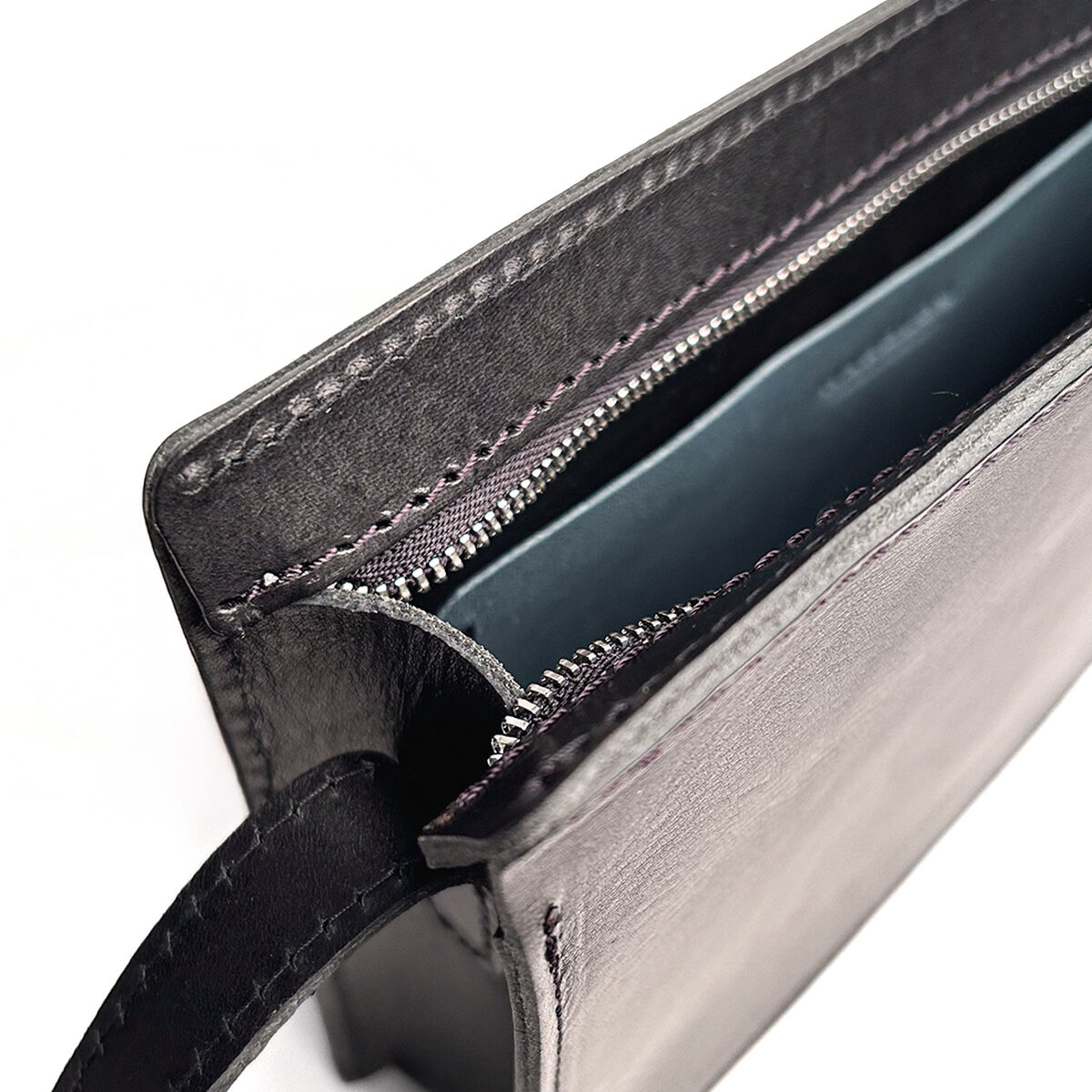 Die Abbildung zeigt eine hochwertige Kernledertasche mit schlichtem, modernem Design in Schwarz. Die Tasche besitzt einen Reißverschluss und ist teilweise geöffnet, sodass das Innenfach sichtbar ist. Das Accessoire wirkt elegant und eignet sich ideal für den täglichen Gebrauch oder besondere Anlässe.