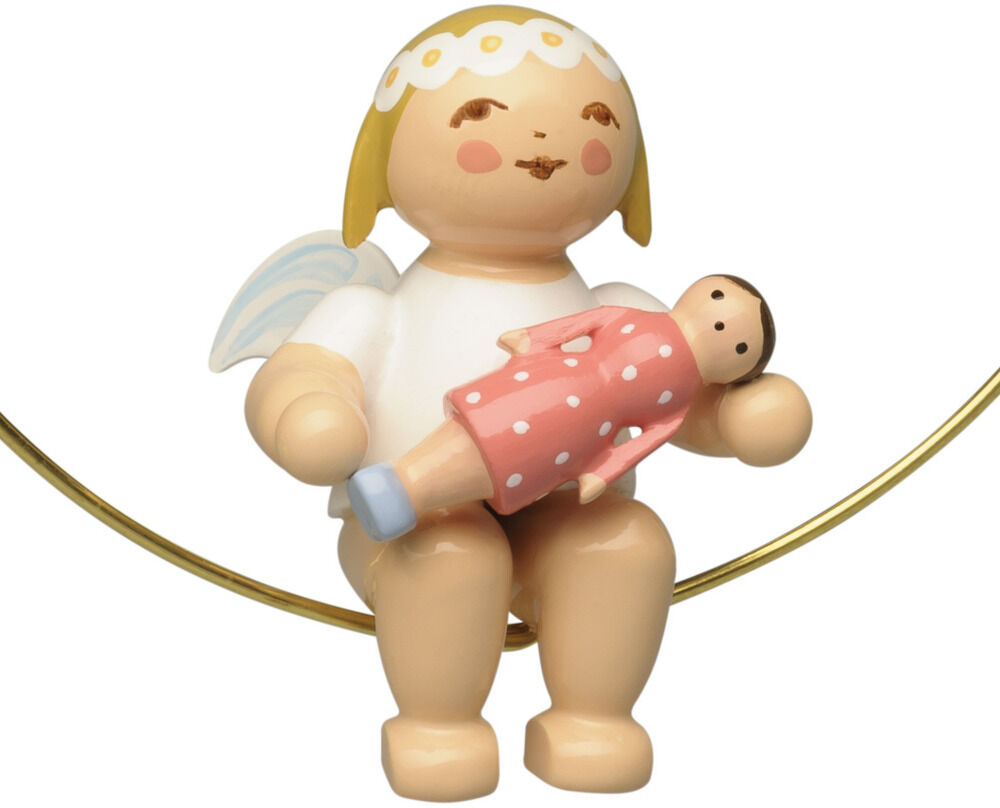Freigestellte Wendt-&-Kühn-Holzfigur: Ein rundlicher Christbaumengel mit weißem Kleid, gelbem Haar und weißer Spitzenhaube sitzt in einem dünnen goldenen Ring. Er hält eine Puppe im korallrosa Kleid mit weißen Punkten und hellblauen Schuhen. Hinter dem Engel sind zart hellblau-weiße Flügel sichtbar.