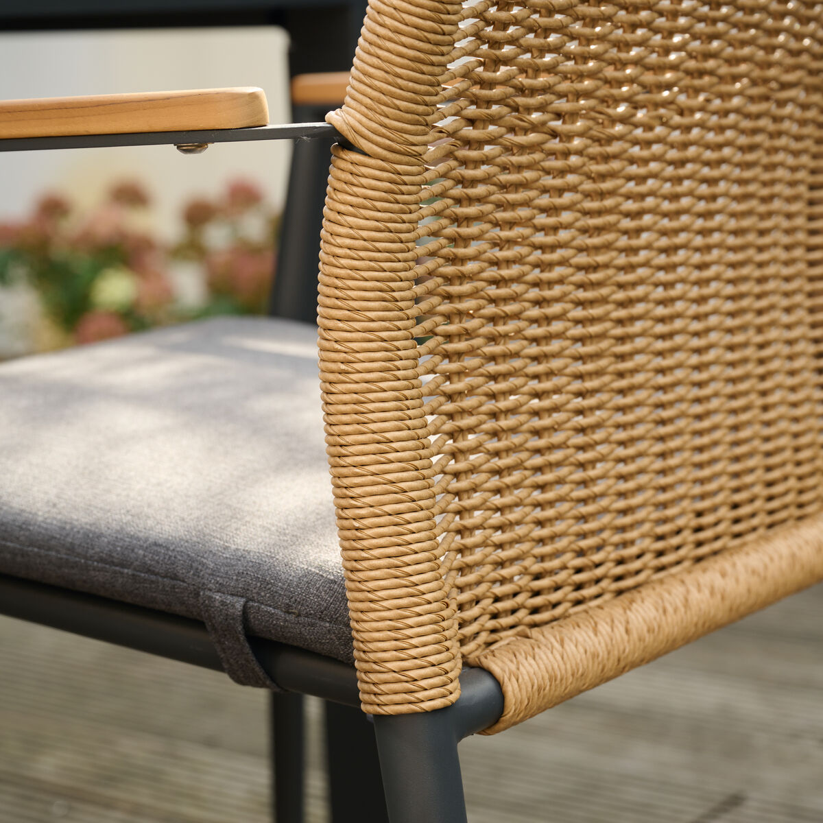 Ein beiger Stapelsessel aus Rattan-Optik mit grauem Sitzpolster und schwarzen metallischen Beinen, geeignet für den Außenbereich auf einer Terrasse.