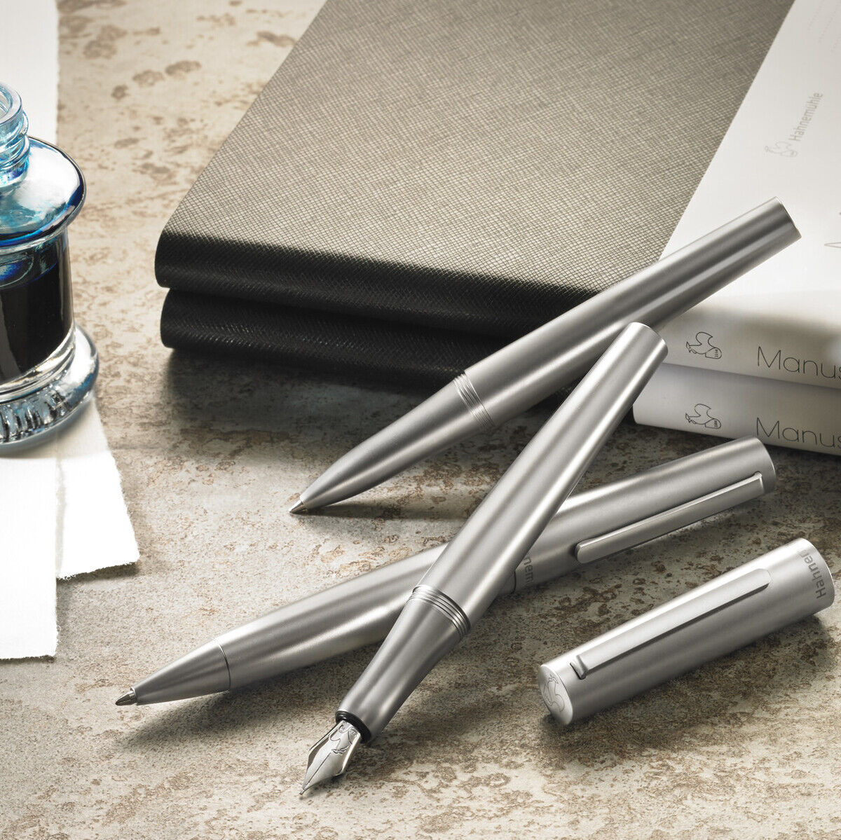 Ein eleganter Kugelschreiber in Silber, der auf einem Schreibtisch neben einem offenen Notizbuch und einem Glas mit schwarzer Tinte liegt. Ideales Geschenk für professionelle oder kreative Anlässe.