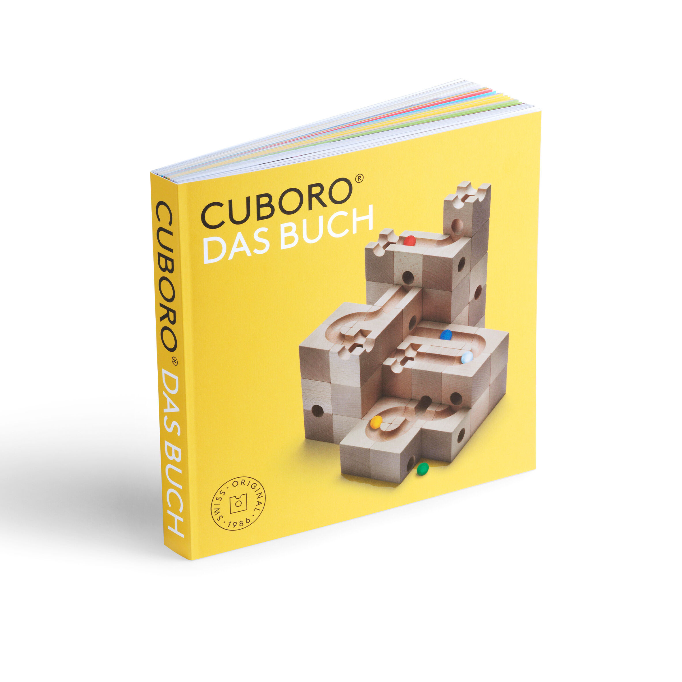 Quadratisches Buch mit gelbem Cover und farbigem Buchschnitt. Titel „CUBORO – DAS BUCH“. Zentral ist eine realistische Darstellung einer aus Holz gefertigten Kugelbahn mit bunten Kugeln abgebildet. Modernes, aufgeräumtes Design, hochwertiger Eindruck.