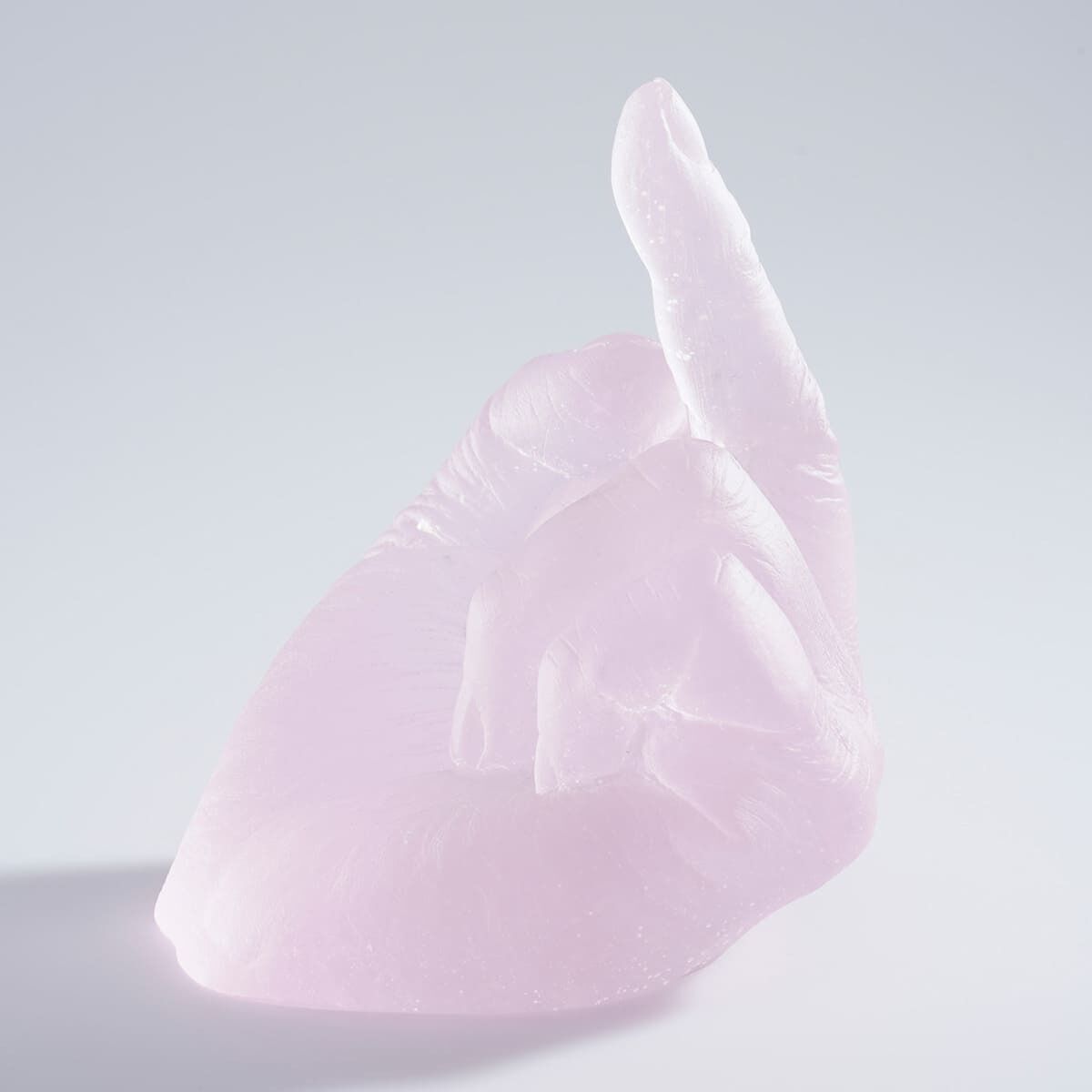 Ein Kunstwerk von Ai Weiwei mit dem Titel 'Study of Perspective in Glass'. Die Skulptur besteht aus Glas und zeigt eine abstrahierte Handgeste in zartem, hellem Rosa. Die Oberfläche ist glatt, und das Werk hat ein minimalistisches Design.