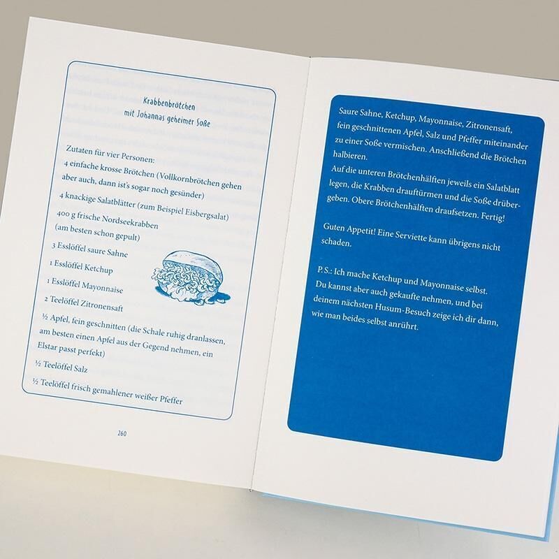 Eine geöffnete Doppelseite eines Buches. Auf der linken Seite ist ein Rezept für 'Krabbenbrötchen mit Joghurtgurkensauce' zu sehen, während auf der rechten Seite das Rezept detaillierter auf blauem Hintergrund beschrieben wird.