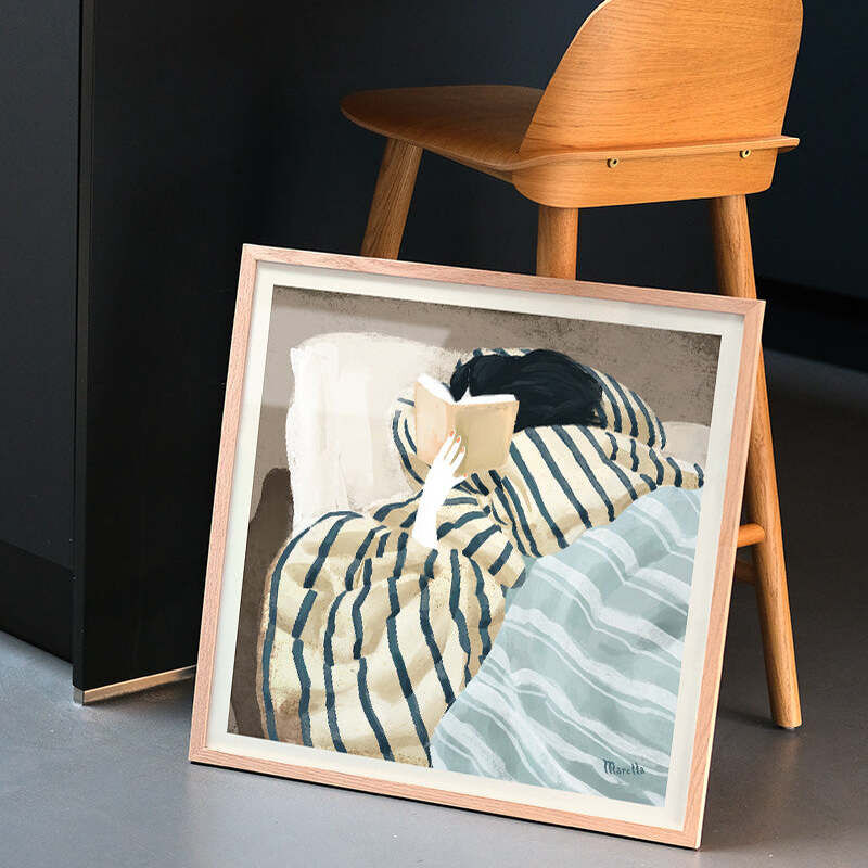 Das gerahmte Poster »Winter Holidays« von Marco Marella zeigt eine minimalistische Illustration einer Person, die im karierten Pyjama gemütlich im Bett liegt und ein Buch liest. Das Bild strahlt Ruhe und winterliche Entspannung aus und steht an eine Holzstuhl gelehnt auf einem glatten, grauen Boden.