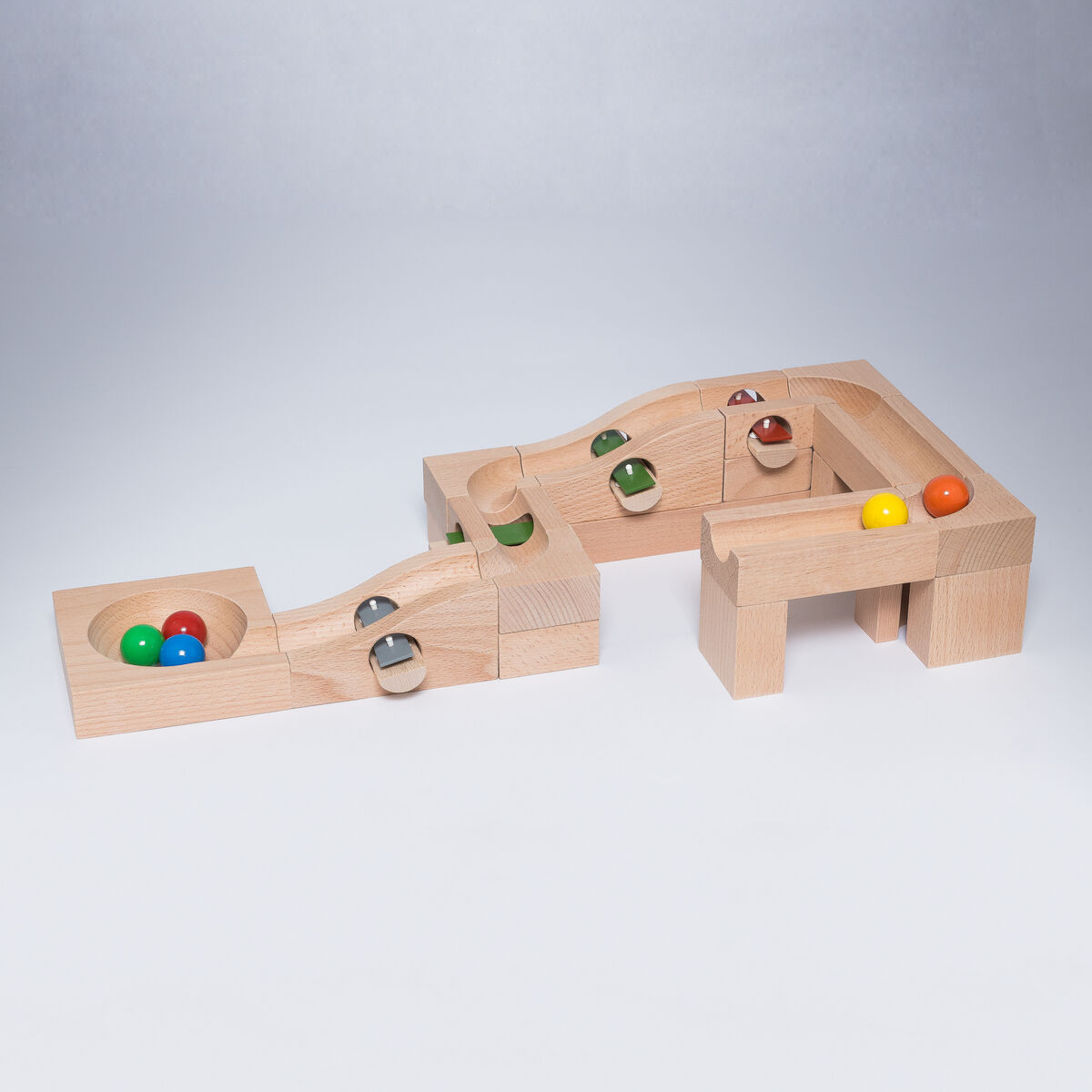 Ein Holzspielzeug mit einer Kugelbahn, bestehend aus geometrischen Blöcken und bunten Murmeln. Die Bahn ist modular aufgebaut und fördert die Kreativität und Motorik von Kindern.