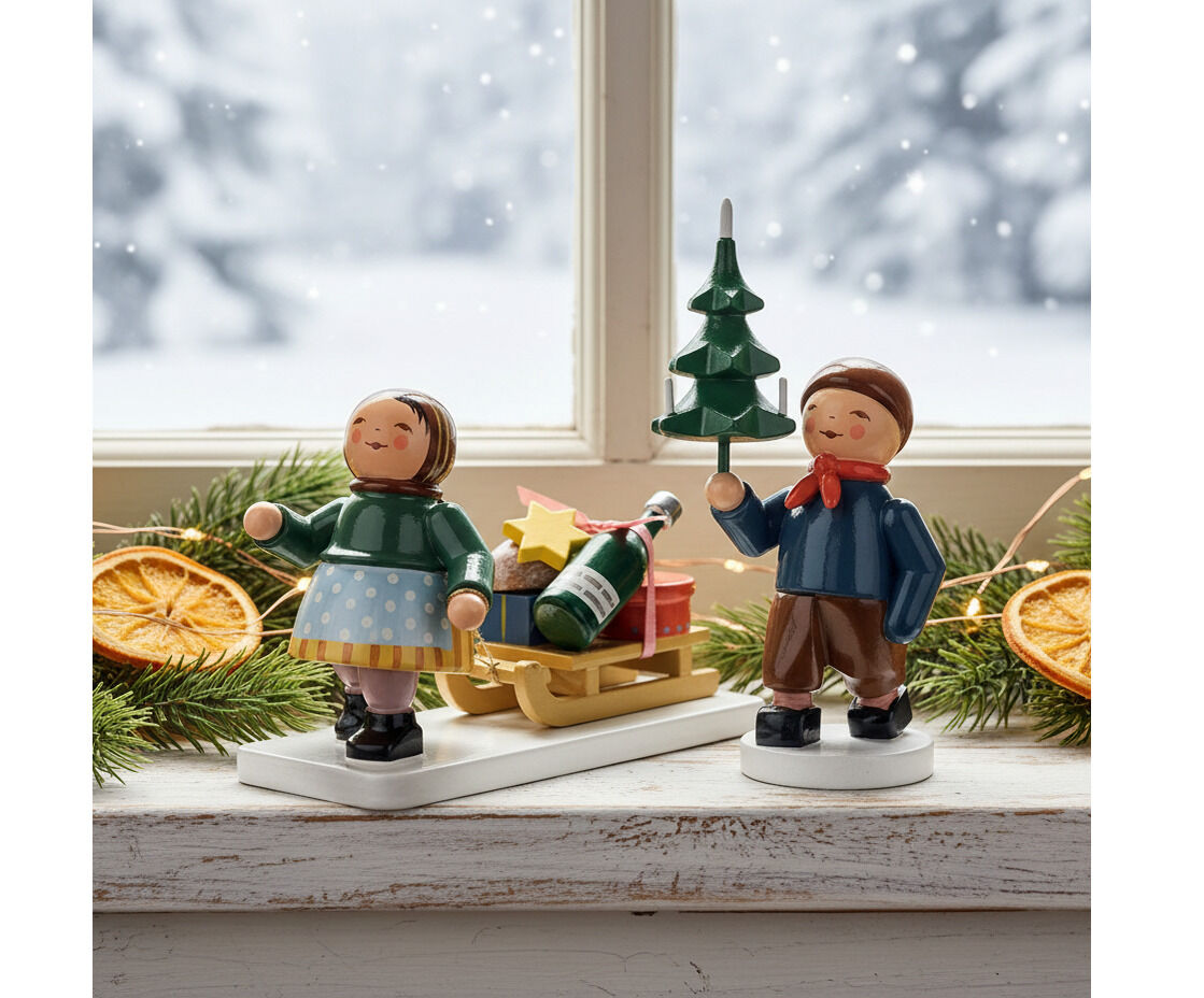 Zwei detailreiche Holzfiguren von Wendt & Kühn stehen auf einer winterlichen Fensterbank. Links ein Mädchen mit grünem Pullover und Schlitten voller Geschenke, rechts ein Junge mit Tannenbaum. Umrahmt von Fichtenästen, getrockneten Orangenscheiben und Lichterkette, Hintergrund: verschneiter Wald.