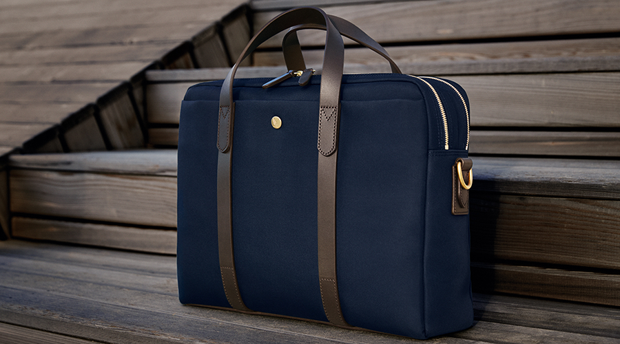 Dunkelblaue Business-Tasche mit braunen Ledergriffen und goldfarbenen Reißverschlüssen auf Holzstufen