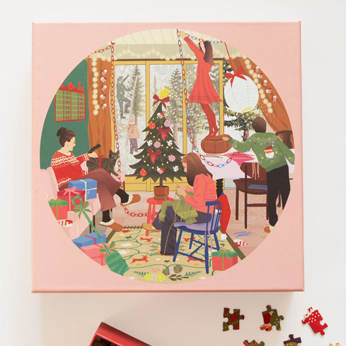 Die Abbildung zeigt die Schachtel eines 1000-Teile-Puzzles mit einer Illustration einer Familie, die ein Wohnzimmer mit einem festlich geschmückten Weihnachtsbaum dekoriert. Im Vordergrund liegen einzelne Puzzleteile und der geöffnete Karton. Im Raum herrscht eine gemütliche, winterliche Stimmung mit Geschenkpapier, Girlanden und winterlicher Szenerie durch ein Fenster im Hintergrund.
