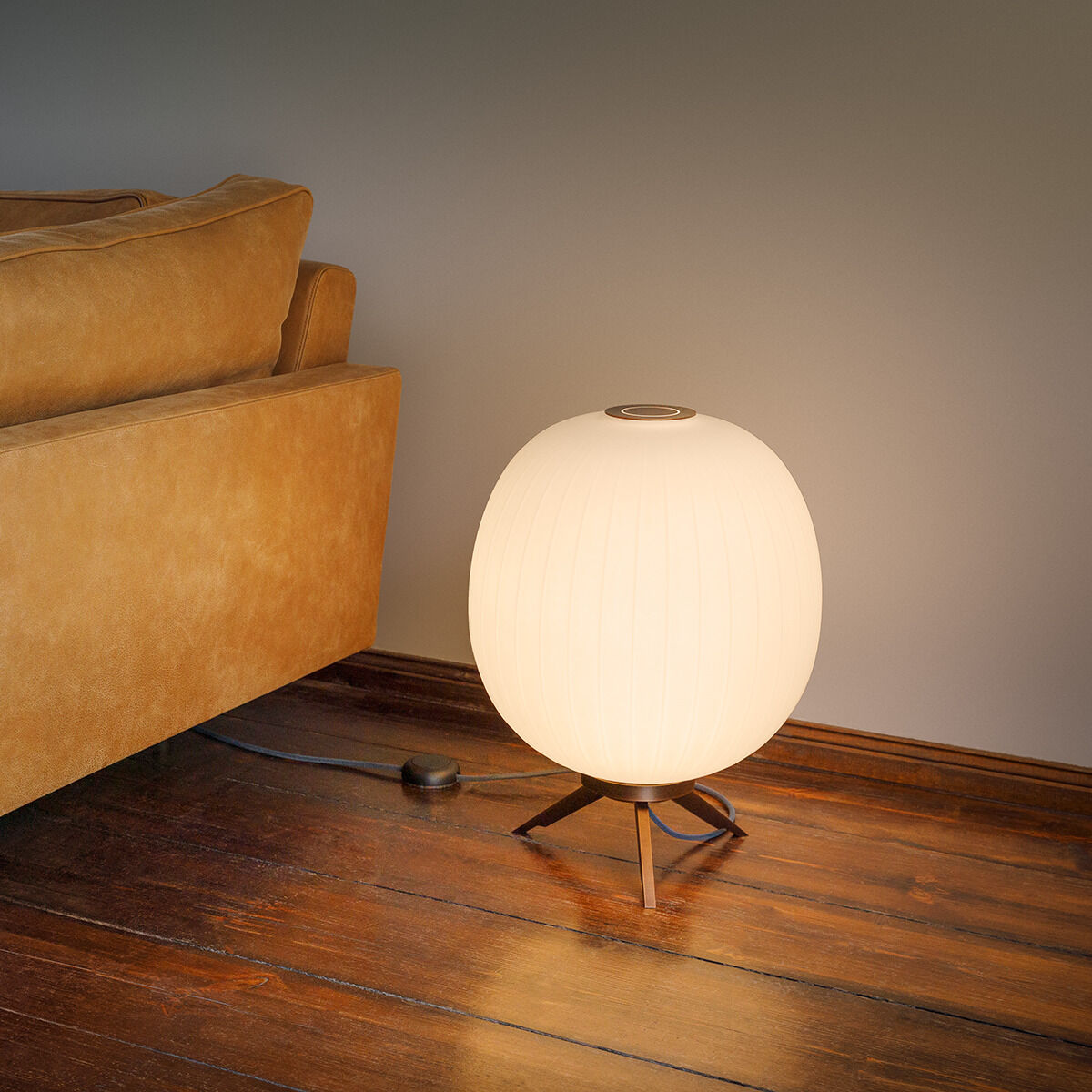 Eine Bodenleuchte namens 'Bologna' steht auf einem Holzboden neben einem beigen Sofa. Die Lampe hat eine kugelförmige, weiße Leuchtkörperstruktur und strahlt ein warmes Licht aus, das eine gemütliche Atmosphäre im Wohnraum schafft.