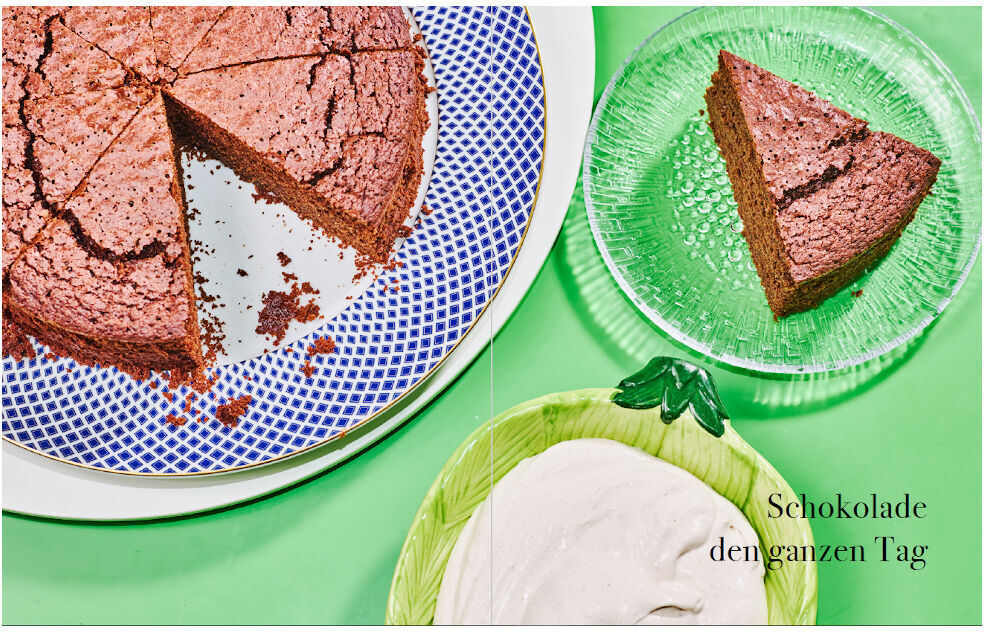 Ein Stück Schokoladenkuchen auf einem grünen Teller, daneben ein großer Schokoladenkuchen auf einem blauen Teller und ein grüner Teller mit einer weißen Creme im Hintergrund. Text auf dem Bild: 'Schokolade den ganzen Tag.'