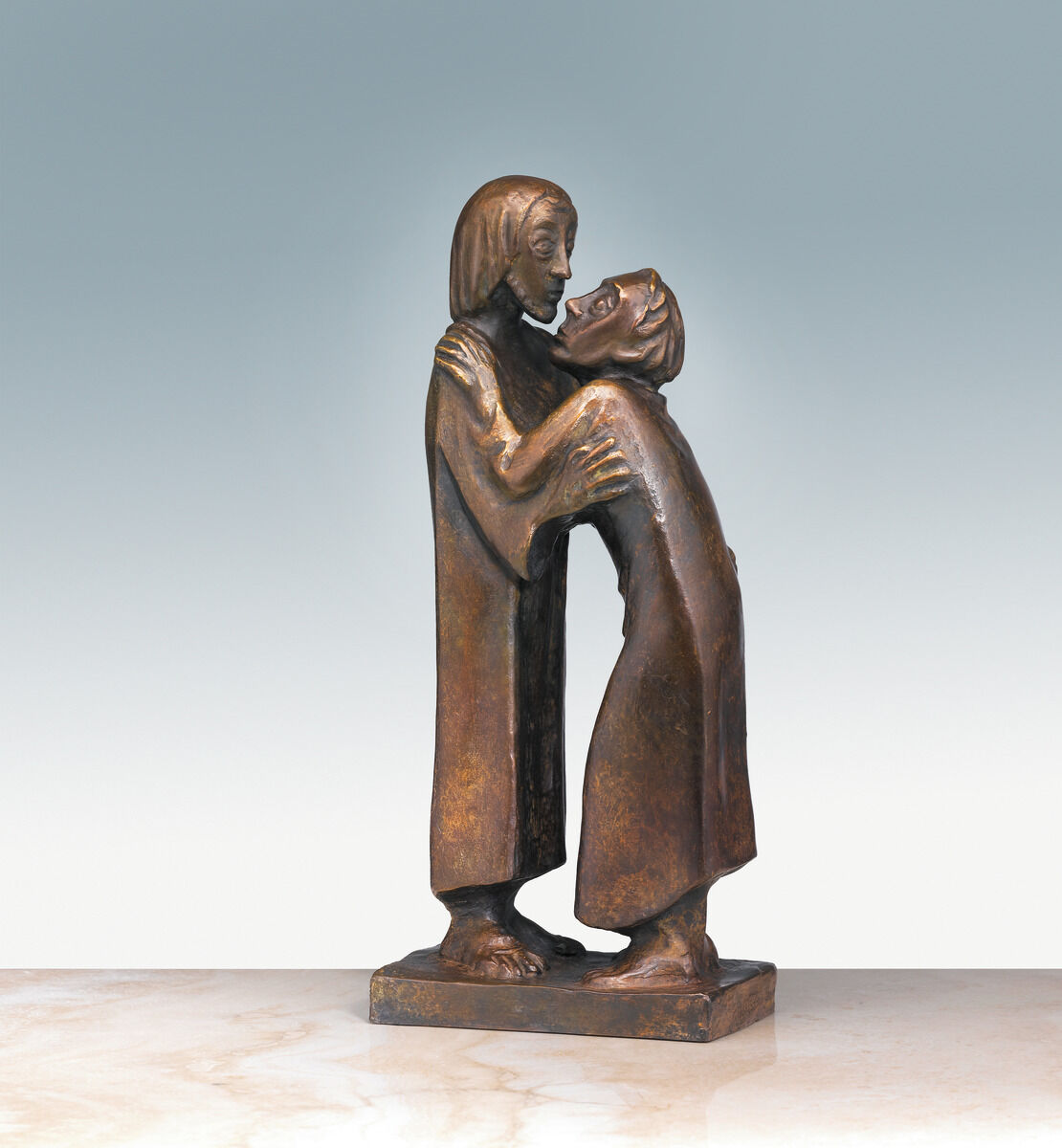 Die Bronzeskulptur »Das Wiedersehen« von Ernst Barlach zeigt zwei Figuren in inniger Umarmung und Berührung. Die Figuren tragen lange Gewänder und stehen aufrecht auf einem rechteckigen Sockel. Der Hintergrund ist ein sanfter Verlauf von Grün zu Weiß.