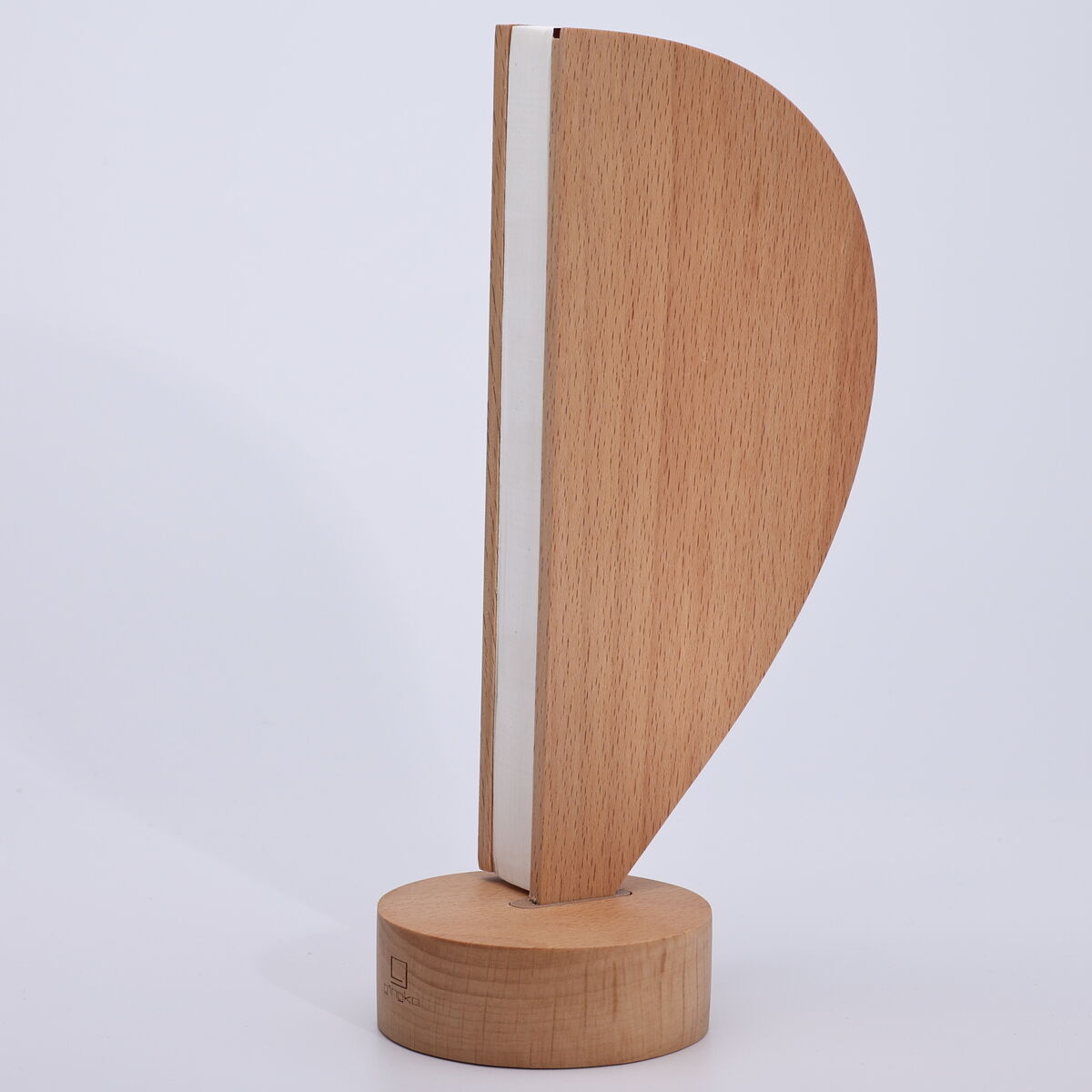 Moderne Tischleuchte »Aeris Light« von Gingko Design Ltd aus Eschenholz in organisch-minimalistischer Form. Die Lampe steht auf einem runden, hölzernen Sockel und besitzt eine vertikale, leicht gebogene Leuchtfläche mit weißem Lichtstreifen. Stilvolles, schlichtes Design für moderne Wohnräume.