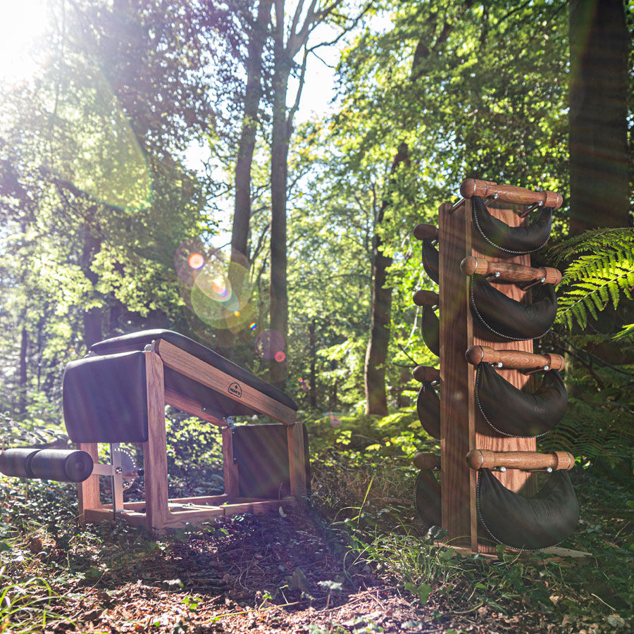 Holzstuhl und Holzregal mit schwarzen Sitzkissen in einem sonnendurchfluteten Wald