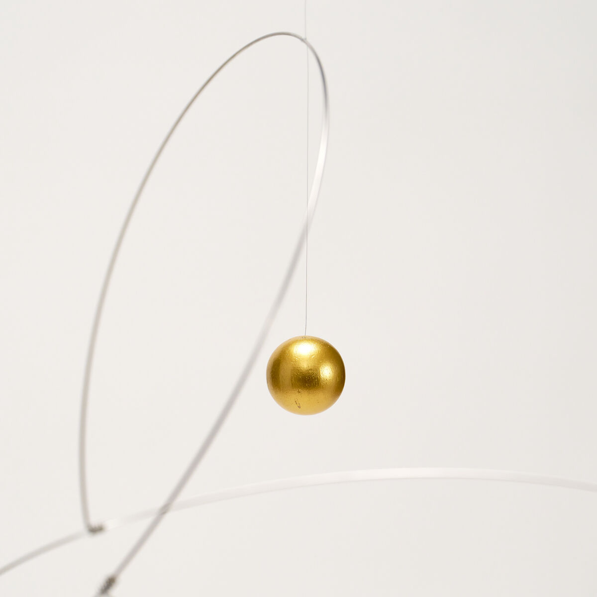 Das Mobile "Metamorphosis, Golden Planet" von Flensted Hanging Art zeigt eine einzelne goldene Kugel, die in einem filigranen silbernen Draht-Gestell hängt. Das schwebende Kunstobjekt wirkt elegant und futuristisch auf weißem Hintergrund.