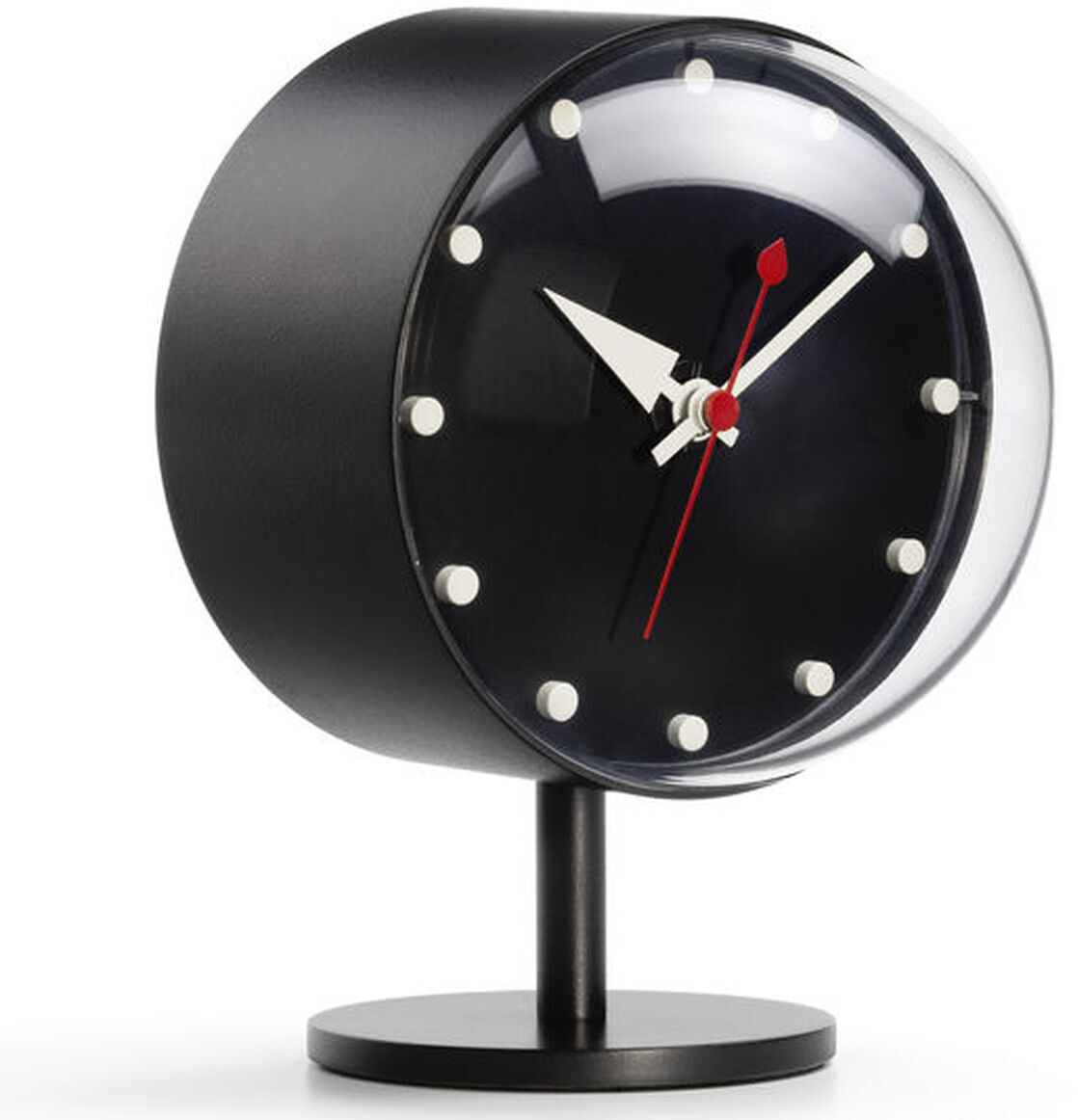 Tischuhr »Night Clock« mit einem runden schwarzen Gehäuse, weißen Zifferblatt-Markierungen und roten Zeigern, auf einem minimalistischen Standfuß platziert.