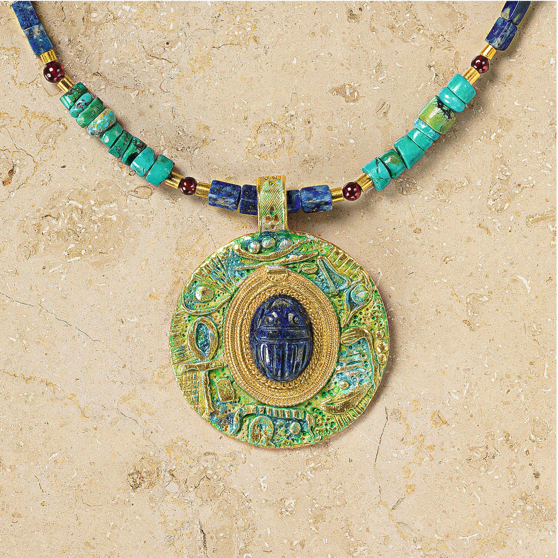 Detailreiche Nahaufnahme des Colliers »Scarabeo« von Petra Waszak für Ars mundi: Der runde Anhänger zeigt einen zentralen Skarabäus aus tiefblauem Lapis, umgeben von türkisen, blauen und roten Steinen sowie glanzvollen Elementen aus 24 Karat vergoldetem Messing. Die Kette ist edel und hochwertig verarbeitet.