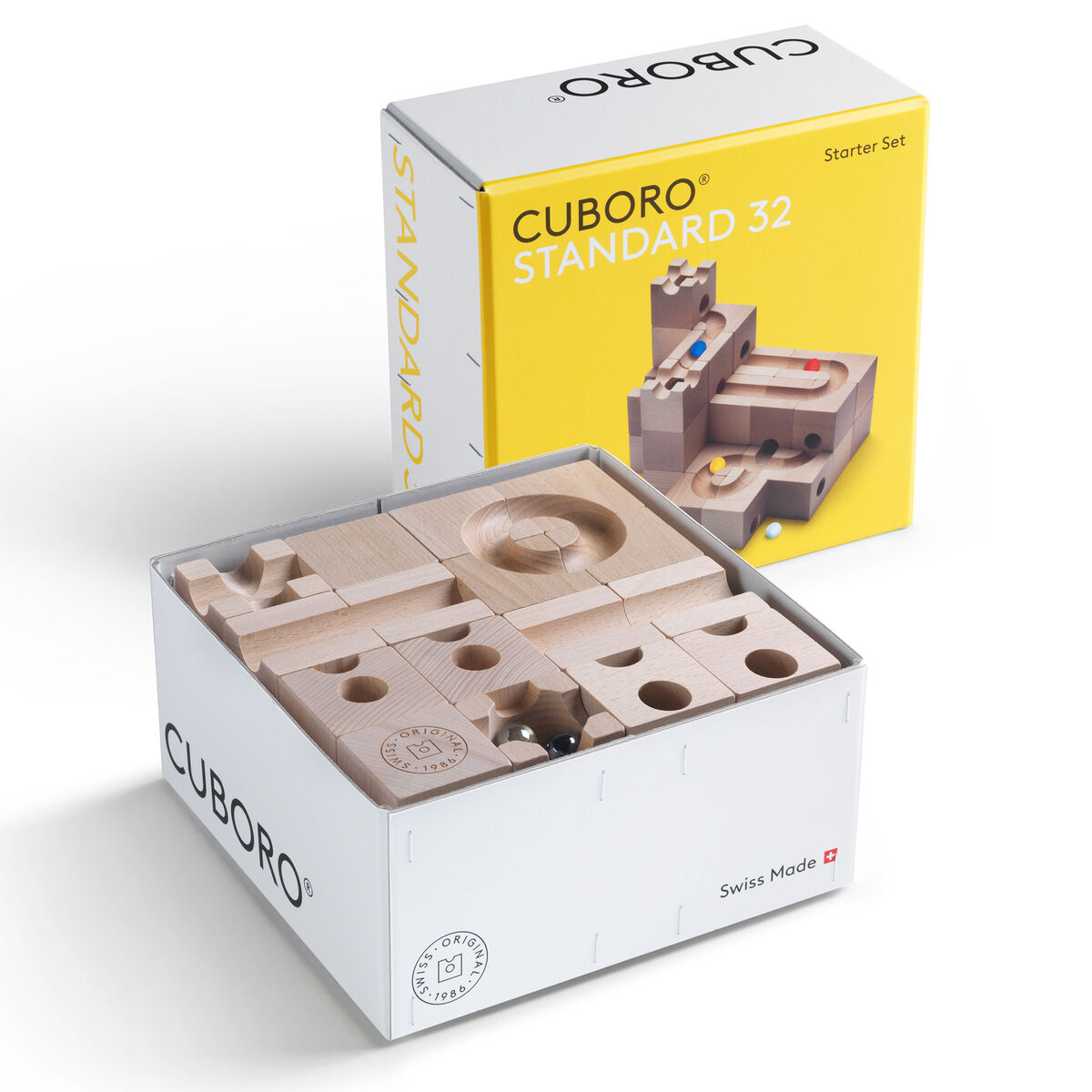 Das Bild zeigt das Cuboro Kugelbahn Starter-Set »STANDARD« mit 32 Holzelementen und fünf Kugeln. Im Vordergrund ist die geöffnete weiße Verpackung mit den naturbelassenen Holzbausteinen sichtbar. Dahinter steht die gelbe, geschlossene Verpackung mit Produktbild und Schriftzug.