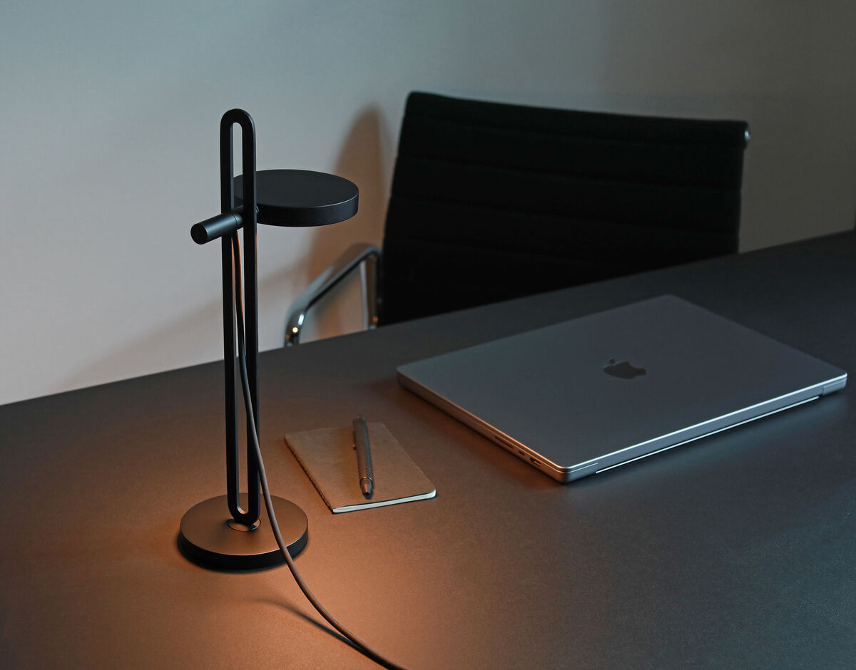 Minimalistische Tischlampe 'Echo' in Schwarz auf einem modernen Bürotisch neben einem Notebook und Notizbuch mit Stift.
