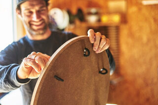 Eine Person hält ein Sensoboard aus Holz in einer Werkstatt. Das Sensoboard hat eine runde Form mit mehreren Griffen.