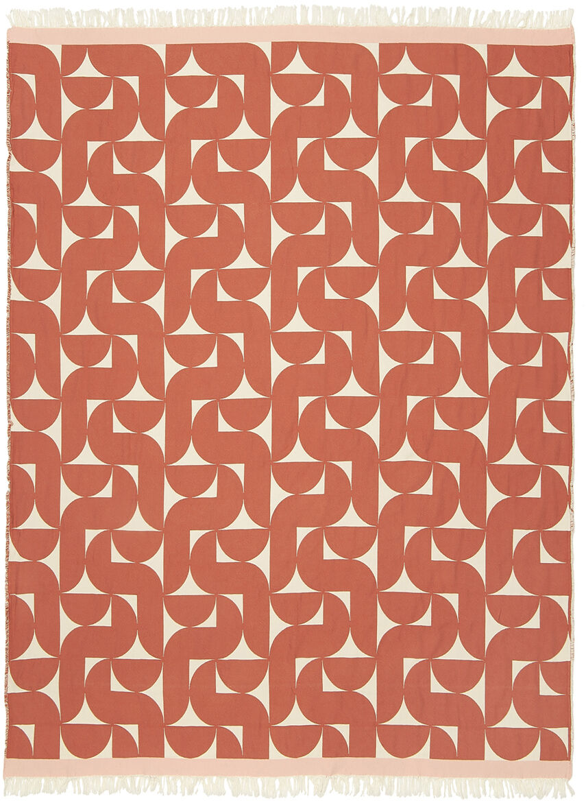 Eine rote Baumwolldecke »Stockholm« mit modernem, geometrischem Muster, zarten Fransen und farbiger Bordüre liegt auf einem hellen Sofa. Die Textur wirkt weich und einladend, das Licht betont die satten Farbtöne und das zeitlose Scandi-Design.