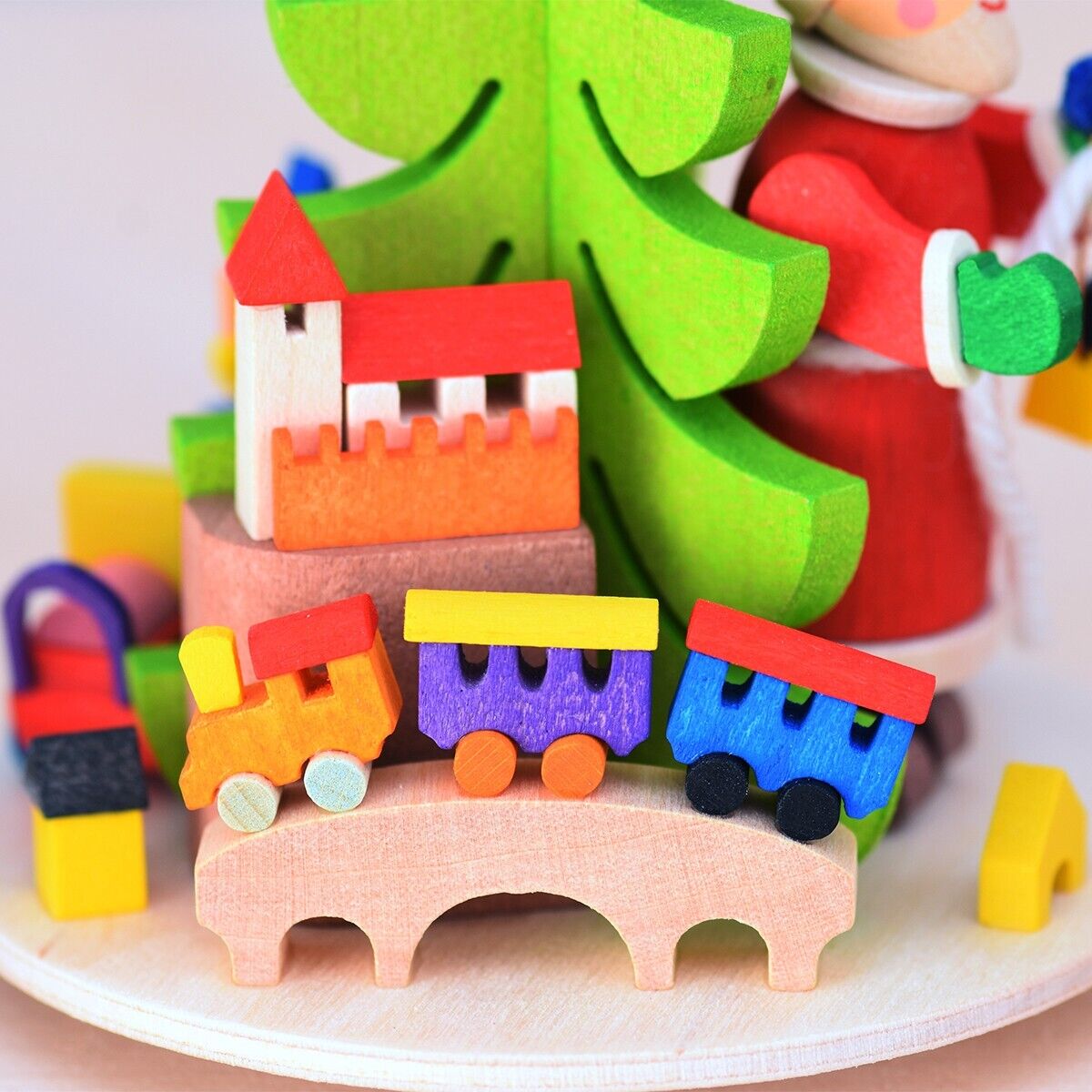 Farbenfrohe Teelichtpyramide mit einem Weihnachtsmann, einem grünen Weihnachtsbaum, bunten Holzhäusern und -spielzeug; basierend auf einem Kreis aus hellem Holz.