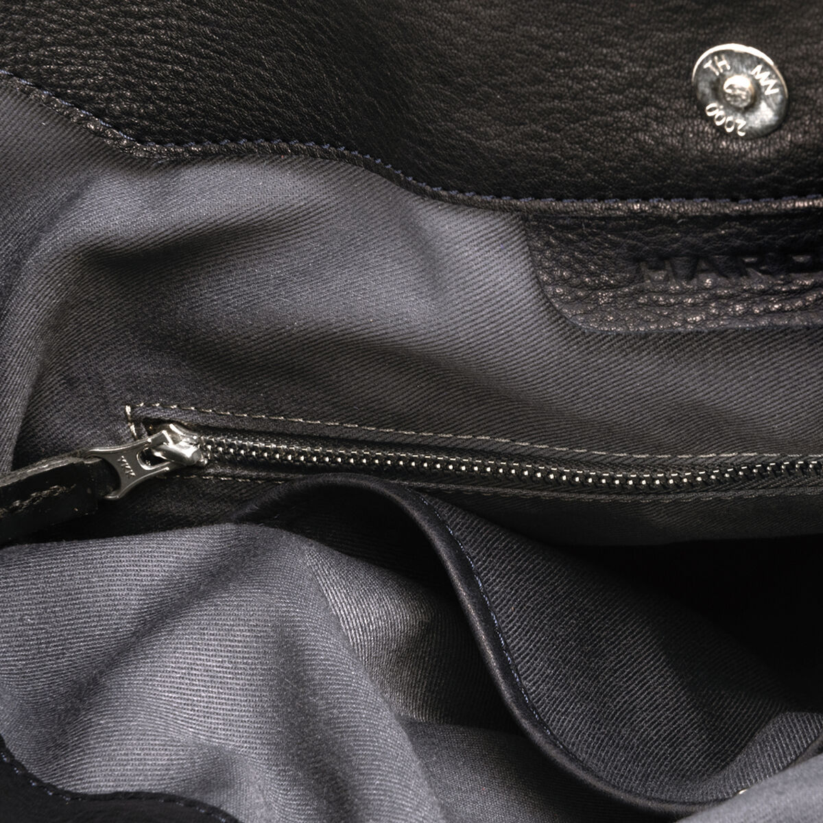Innenansicht einer Beuteltasche »Chaza Pouch Upend« mit grauem Stofffutter, einem Reißverschlussfach und einem Druckknopfverschluss. Die Tasche besteht aus schwarzem Leder.