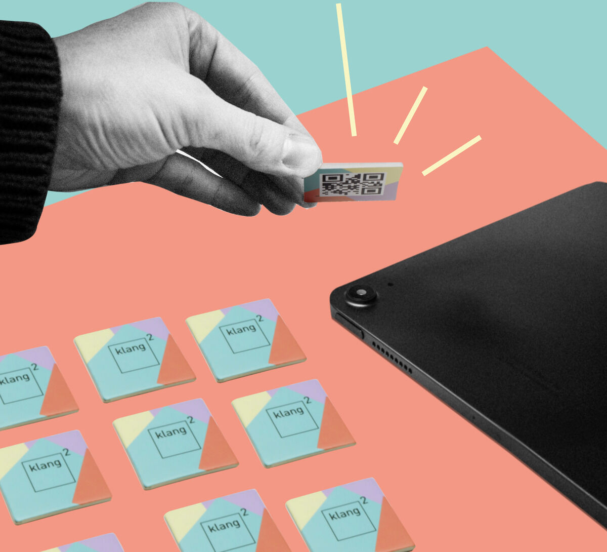 Eine Hand hält eine QR-Karte über ein schwarzes Tablet. Im Hintergrund sind mehrere bunte Spielkarten mit dem Text 'klang²' und Fragezeichen abgebildet.