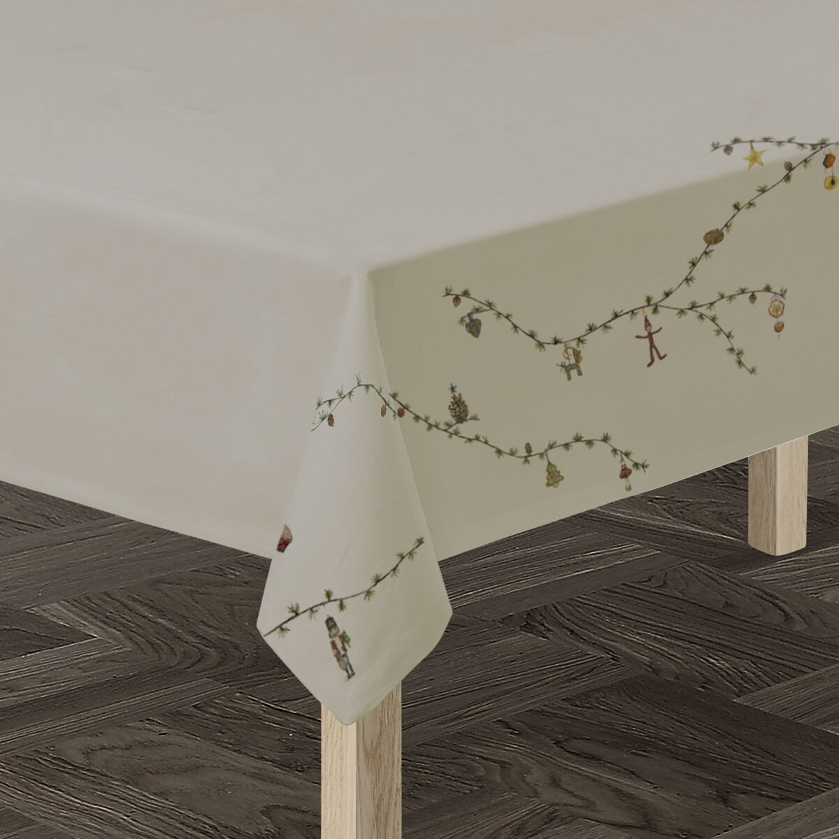 Beigefarbene Tischdecke mit zartem Blumen- und Naturmuster, drapiert über einen rechteckigen Holztisch auf dunklem Holzboden. Die Tischdecke verleiht dem Raum eine elegante und freundliche Atmosphäre und eignet sich besonders für festliche oder familiäre Anlässe.