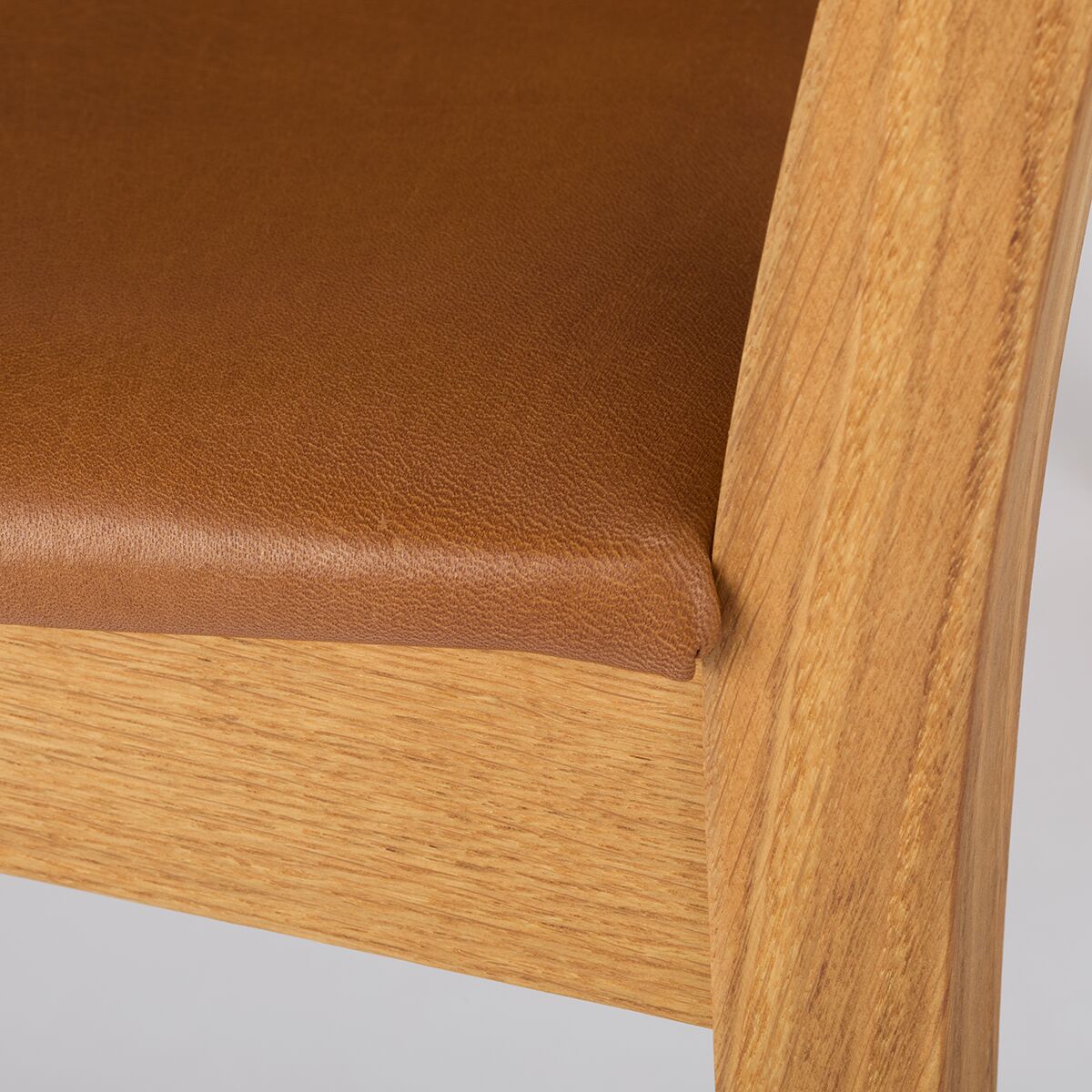 Nahaufnahme von einem Armlehnstuhl mit lederbezogener Sitzfläche und einem Gestell aus hellem Holz.