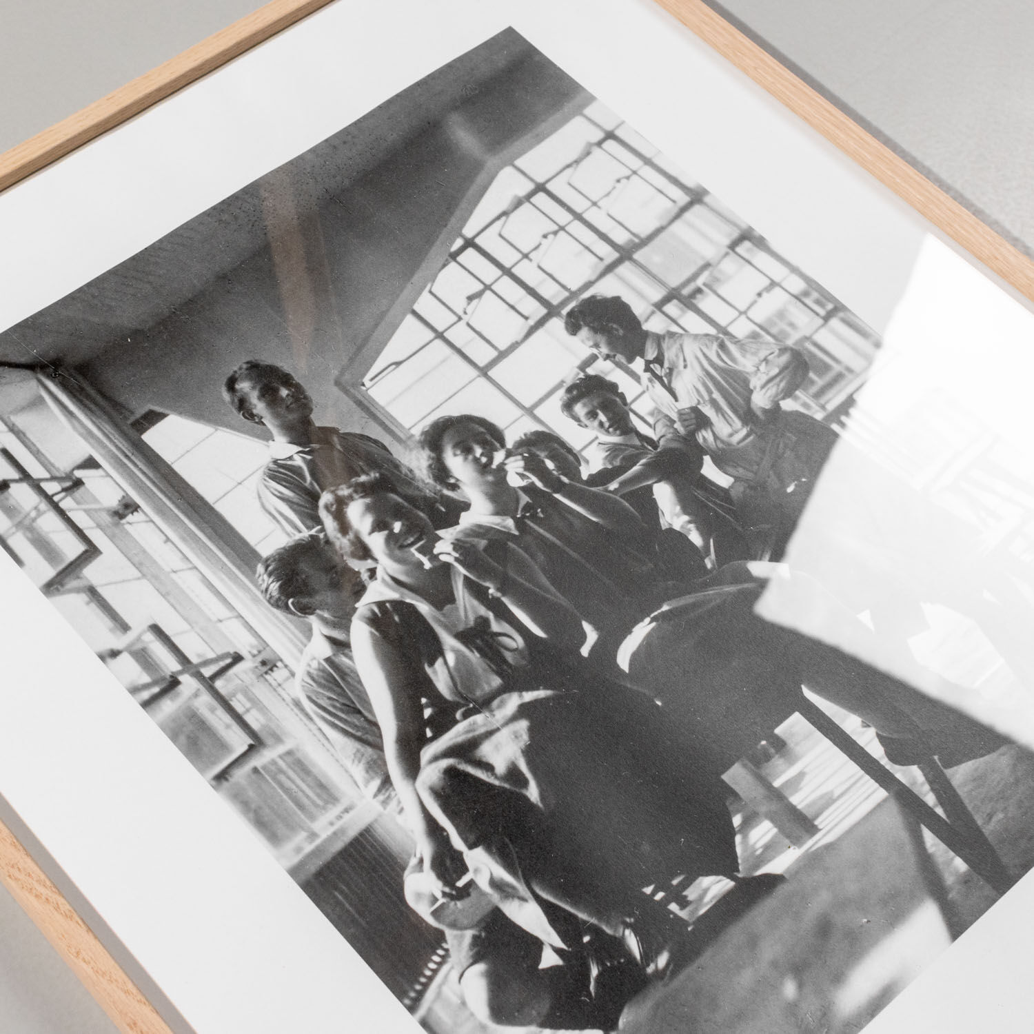 Schwarzweißfotografie in einem Holzrahmen zeigt eine Gruppe von Menschen im historischen Bauhaus Archiv Berlin im Jahr 1928. Das Bild ist minimalistisch und von moderner Architektur umgeben, ideal für Kunstliebhaber und Freunde der Designgeschichte.
