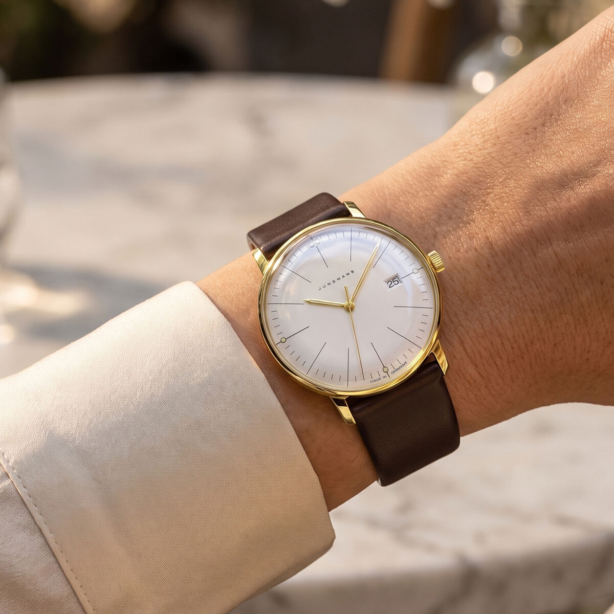 Die ZEIT-Sonderedition »max bill Damen« Uhr der Marke Junghans ist am Handgelenk einer Person zu sehen. Das Modell besitzt ein matt sandgoldenes Edelstahlgehäuse, ein feinsilberfarbenes Zifferblatt, ein dunkelbraunes Lederarmband und wirkt elegant und hochwertig inszeniert.
