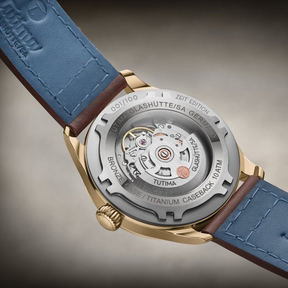 Detailaufnahme der Rückseite einer hochwertigen Automatikuhr der ZEIT-Sonderedition »Flieger Automatic Bronze« mit sichtbarem Uhrwerk durch den Saphirglasboden und blauem Lederarmband. Die Gravur betont die Limitierung und die deutsche Herkunft des Zeitmessers.