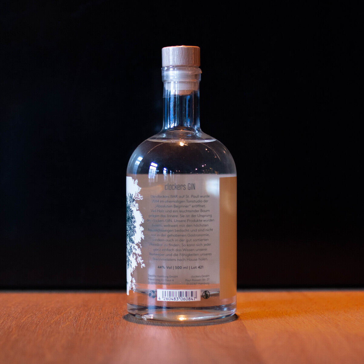 Eine klare Ginflasche der Marke 'clockers Gin St. Pauli' steht auf einem Holztisch vor einem schwarzen Hintergrund. Das Etikett ist teilweise sichtbar.