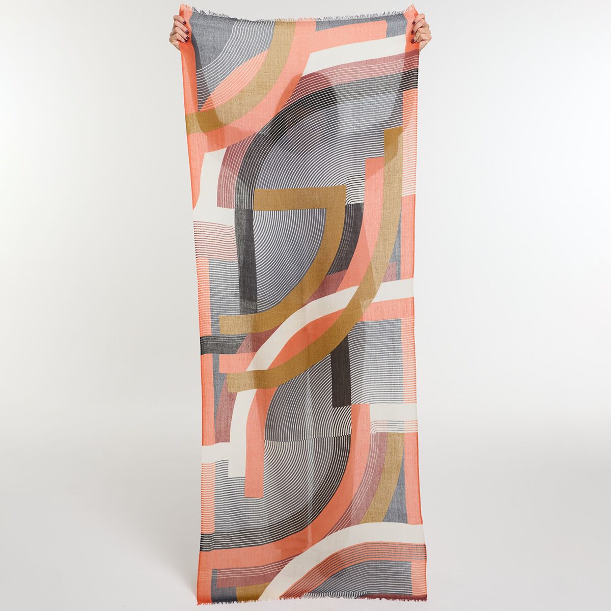 Langer, moderner Wollschal mit geometrischem Muster in Orange-, Rot-, Beige-, Rosa- und Schwarztönen, ausgebreitet vor neutralem Hintergrund mit sichtbarer Struktur und feinen Linien. Geeignet als modisches Accessoire für Herbst und Winter.