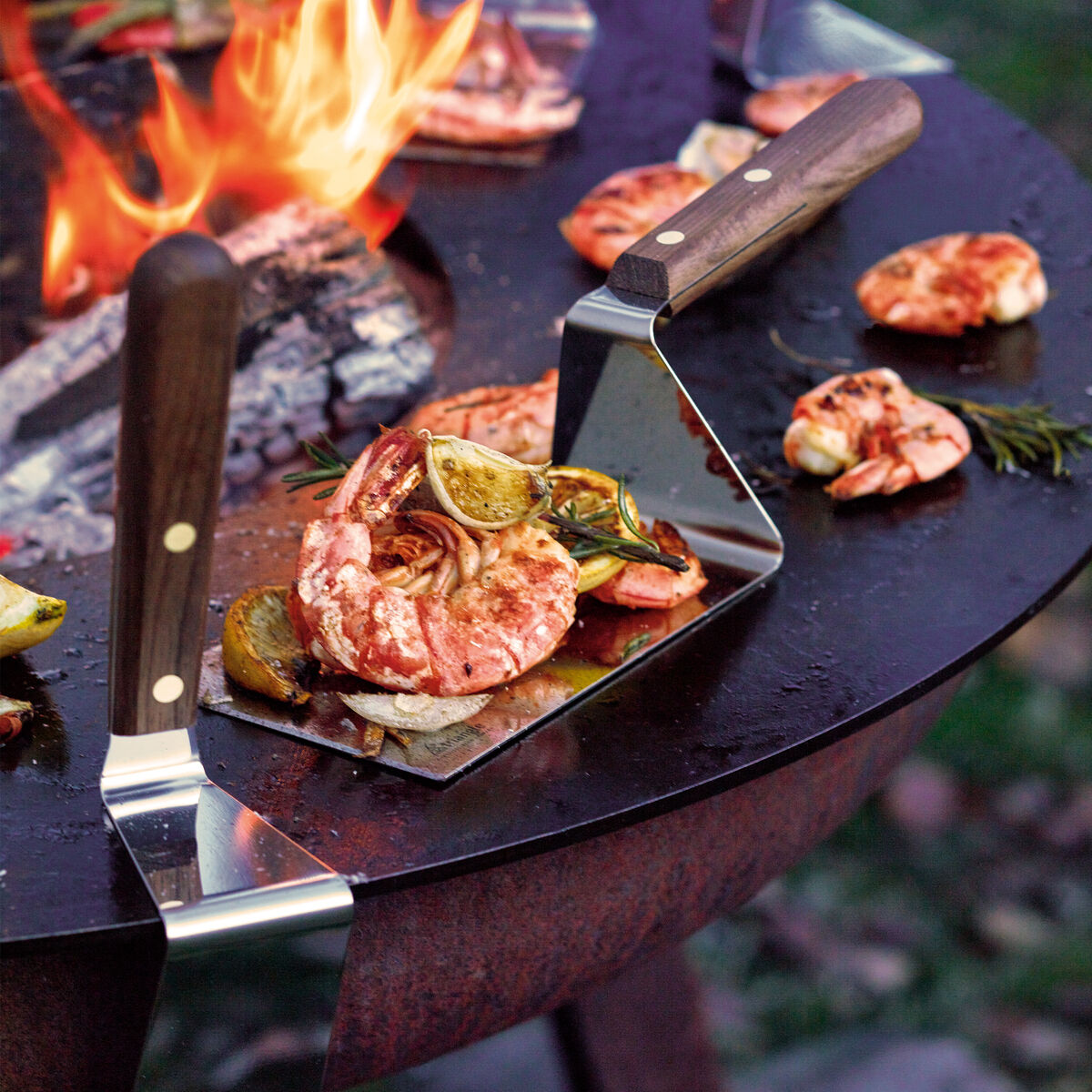 Auf dem Bild ist eine hochwertige Plancha Palette von triangle aus Nussbaumholz und Edelstahl zu sehen. Der Holzgriff ist 15 cm lang, glatt poliert und elegant dunkelbraun, die breite Klinge aus silberfarbenem Metall. Die Szenerie wirkt stilvoll und modern.