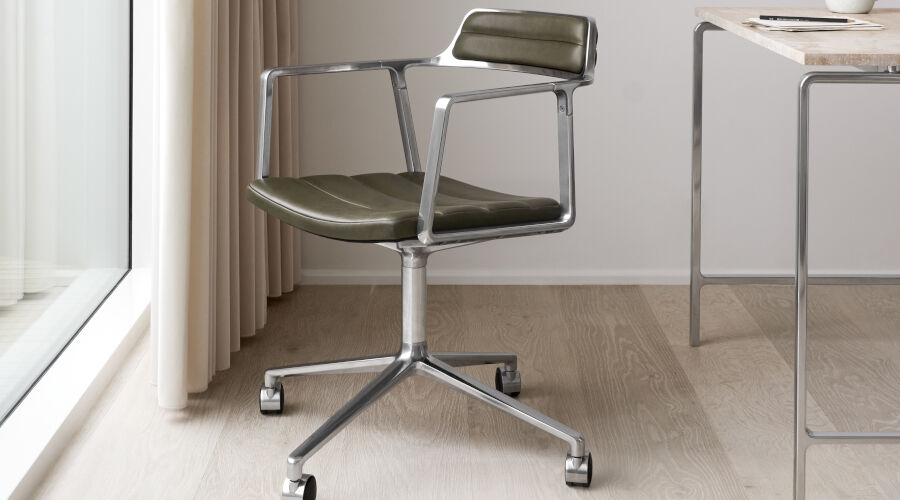 Moderner Schreibtischstuhl mit grünem Polster und verchromtem Gestell neben einem Schreibtisch im Homeoffice