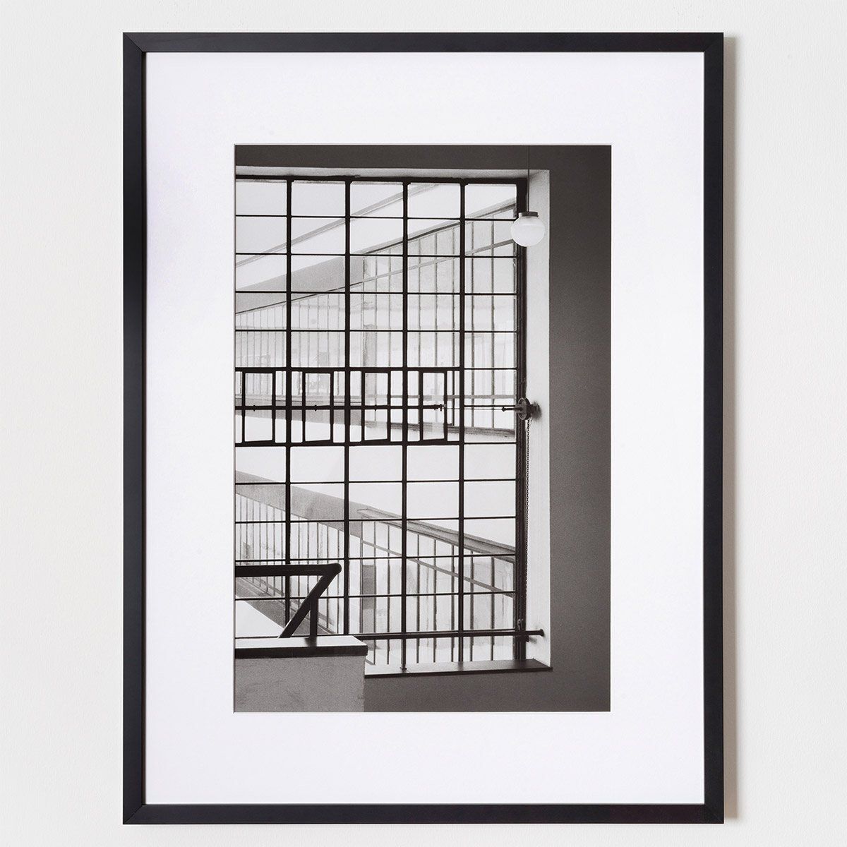 Schwarz-Weiß-Fotografie von Klaus Kinold aus dem Jahr 1992, die den Blick vom Treppenhaus nach außen im Bauhaus Dessau zeigt, entworfen von Walter Gropius. Das Bild betont die geometrischen Formen und Linien des modernen architektonischen Designs.