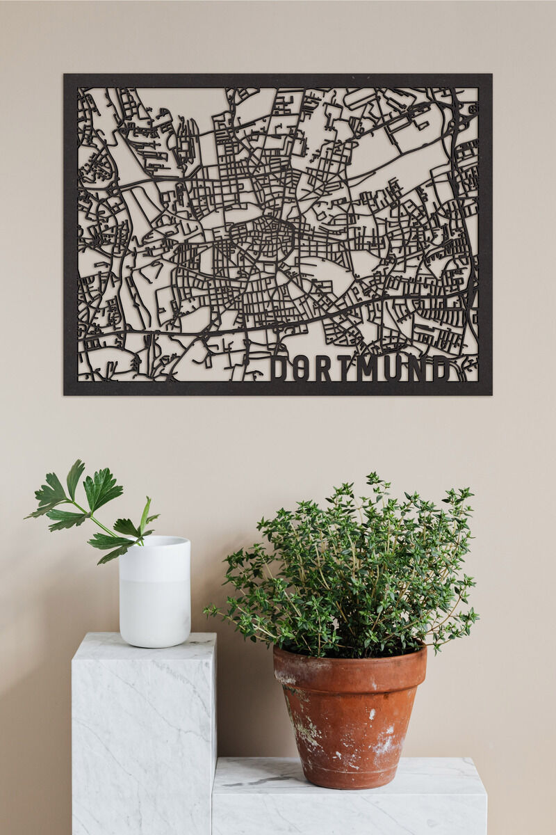 Holzschnitt einer Stadtkarte von Dortmund, montiert auf eine beige Wand, mit einem weißen, zylindrischen Behälter und einem kleinen Topf mit einer grünen Pflanze auf einem weißen Würfel im Vordergrund.
