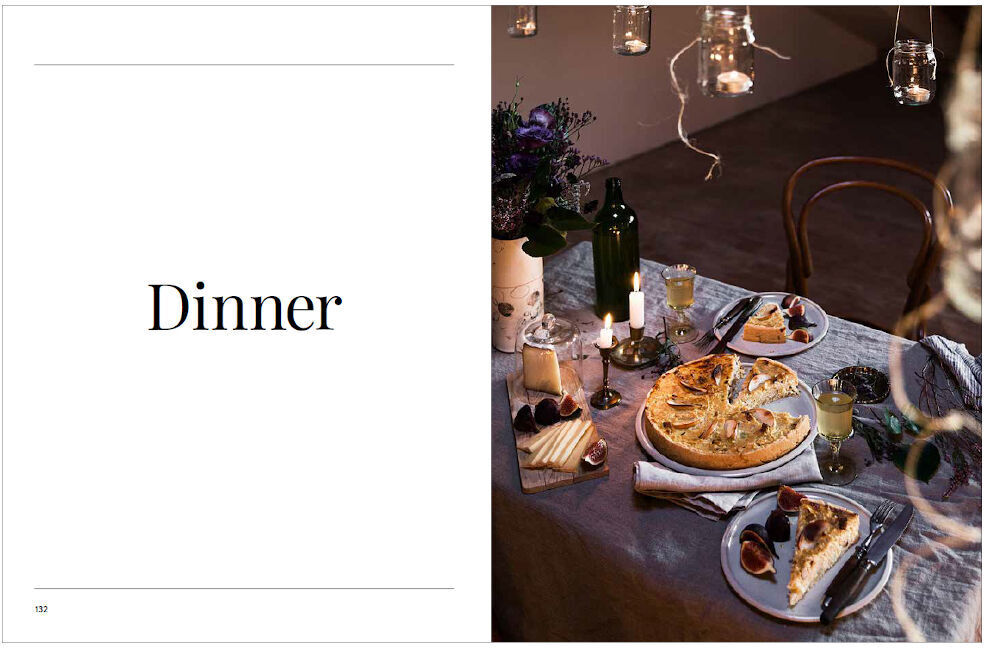 Eine Doppelseite eines Kochbuchs zeigt links den Schriftzug 'Dinner' und rechts ein gedeckter Esstisch mit einer Tarte, einer Weinflasche, Gläser, Kerzen und Blumen.