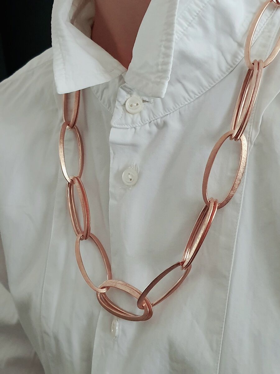 Eine goldene HML-Collier-Halskette »GRACE« mit großen, ovalen Gliedern, getragen von einer Person mit einem weißen Hemd.