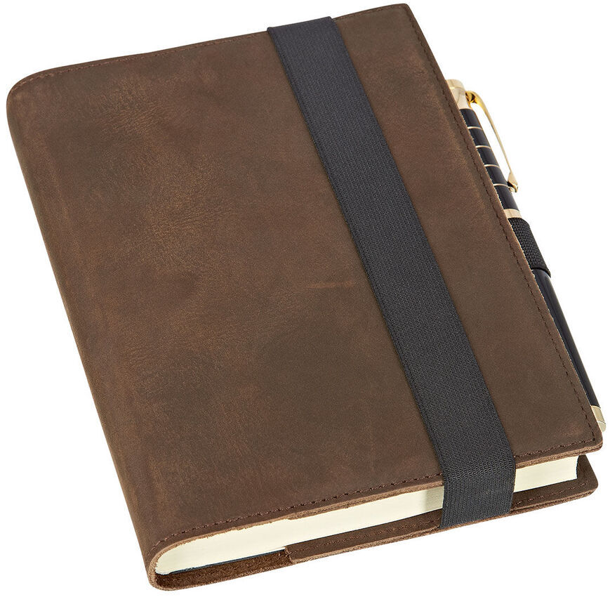 Ein braunes Notizbuch »Travel« in Lederoptik mit einem schwarzen elastischen Verschlussband. Das Notizbuch hat einen Stifthalter, der einen goldfarbenen Stift hält. Geeignet für Reisen, Organisation und Planung.