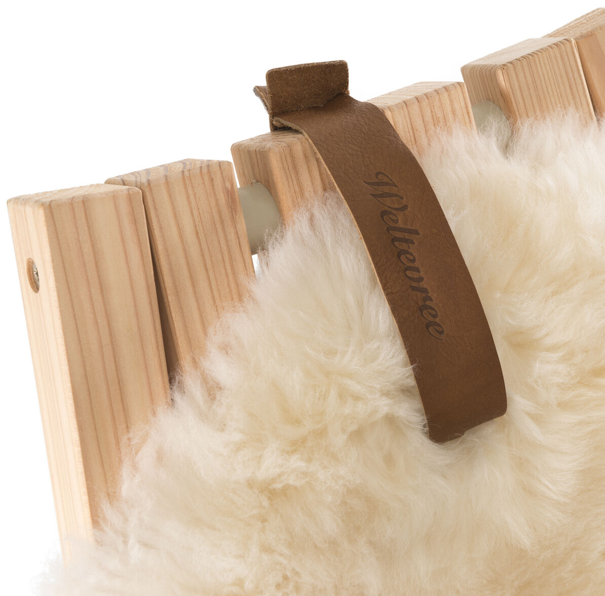 Ein cremeweißes Schafsfell mit einer braunen Lederschlaufe liegt dekorativ über einer naturbelassenen Holzlehne. Das Bild vermittelt ein Gefühl von Gemütlichkeit und Wärme, ideal als Wohnaccessoire.