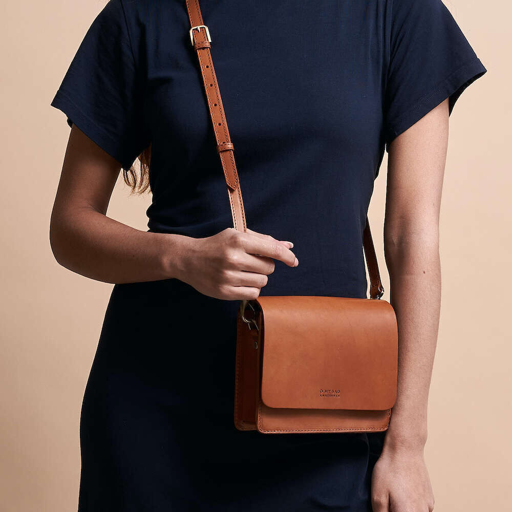 Frau in dunkelblauem Kleid trägt eine kleine braune Apfelledertasche »Audrey Mini« über der Schulter. Tasche aus nachhaltigem veganem Material.
