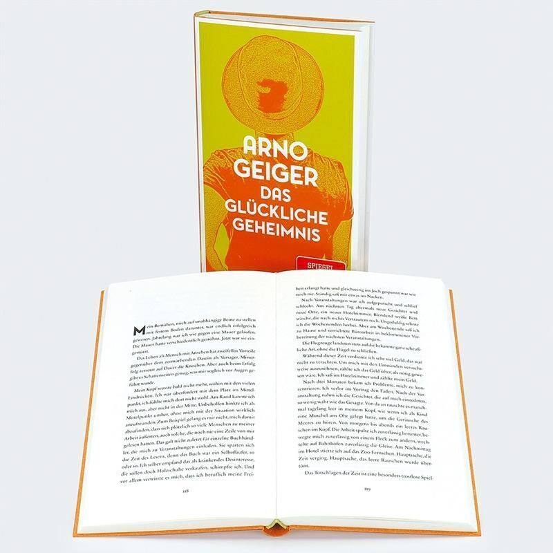 Ein Buch mit dem Titel 'Das glückliche Geheimnis' von Arno Geiger. Der Buchumschlag ist in gelb und orange gehalten und zeigt eine Person, die von hinten zu sehen ist. Das Buch ist geöffnet und zeigt Text auf den Seiten.