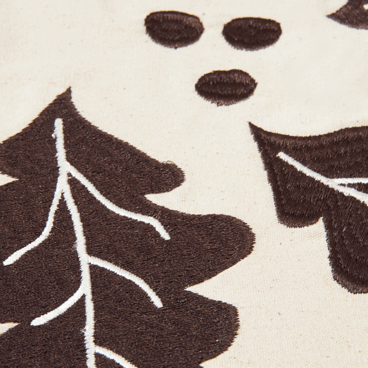 Detailansicht einer Christbaumdecke aus Stoff mit braunen, gestickten Eichenblättern und cremefarbenem Hintergrund. Die Decke zeigt ein naturinspiriertes, handgefertigtes Design mit weißen Akzenten auf den Blättern.