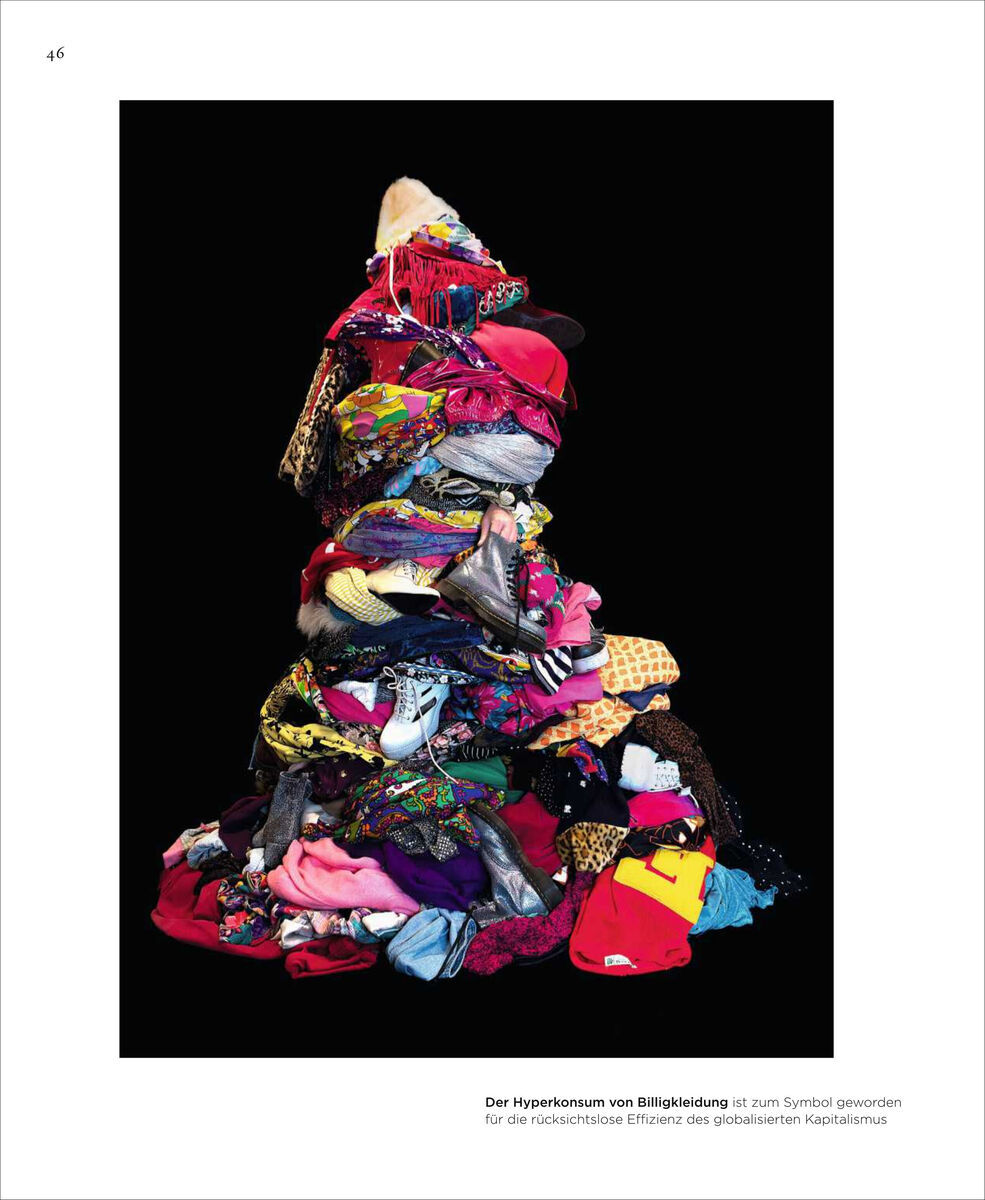 Ein hoher Stapel von bunter Billigkleidung vor schwarzem Hintergrund symbolisiert die exzessiven Auswirkungen des globalisierten Kapitalismus. Text darunter: "Der Hyperkonsum von Billigkleidung ist zum Symbol geworden für die exzessive Entfesselung des globalisierten Kapitalismus."