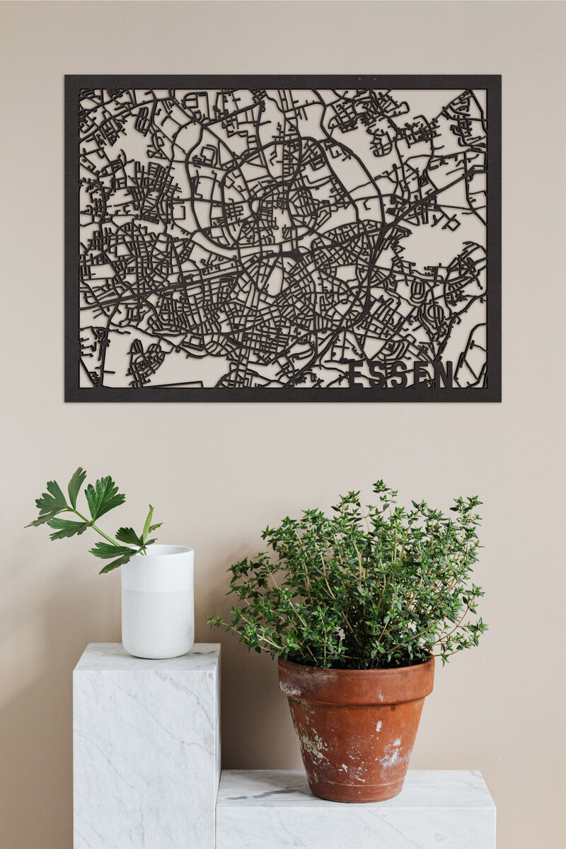 Ein Holzstadtplan von Essen, befestigt an einer beigen Wand. Im Vordergrund befinden sich eine Pflanze in einem Terrakottatopf und eine weiße, zylindrische Vase auf weißen, marmorierten Sockeln.