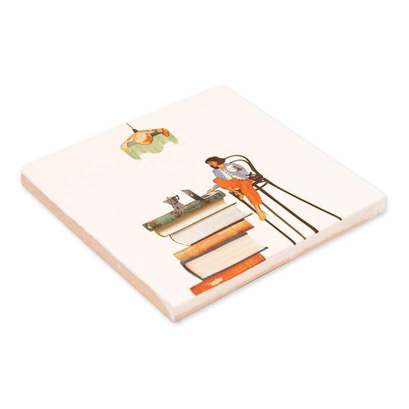 Keramikfliese mit Illustration einer Person, die an einem Schreibtisch auf einem Stapel Bücher sitzt und arbeitet. Darüber hängt eine grüne Lampe. Die Szene ist modern und stilisiert auf einem weißen Hintergrund dargestellt.