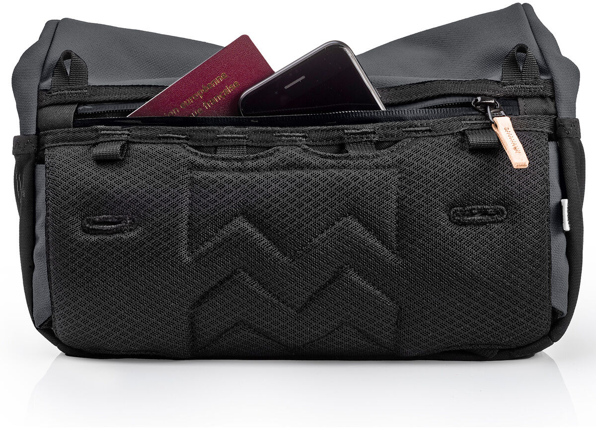 Eine schwarze Umhängetasche namens »Piha« mit mehreren Reißverschlussfächern, in denen man einen Reisepass und ein Smartphone sehen kann. Die Tasche hat ein strapazierfähiges, minimalistisches Design und ist für den täglichen Gebrauch sowie für Reisen geeignet.