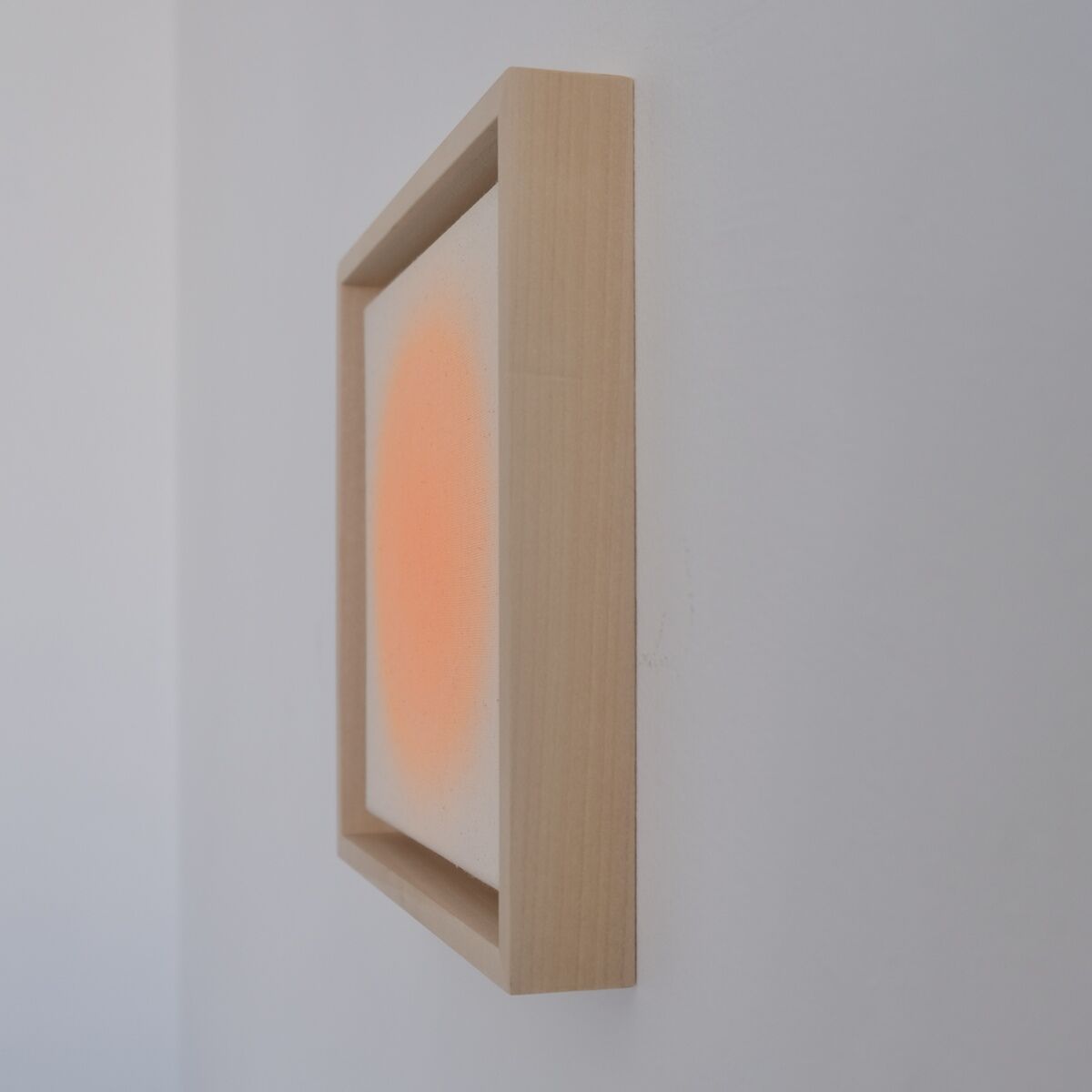 Seitlich aufgenommenes, gerahmtes Kunstwerk mit einem sanften orangenen Farbverlauf auf weißem Hintergrund, aufgehängt an einer weißen Wand. Das schlichte Design unterstreicht den minimalistischen und modernen Stil des Bildes.
